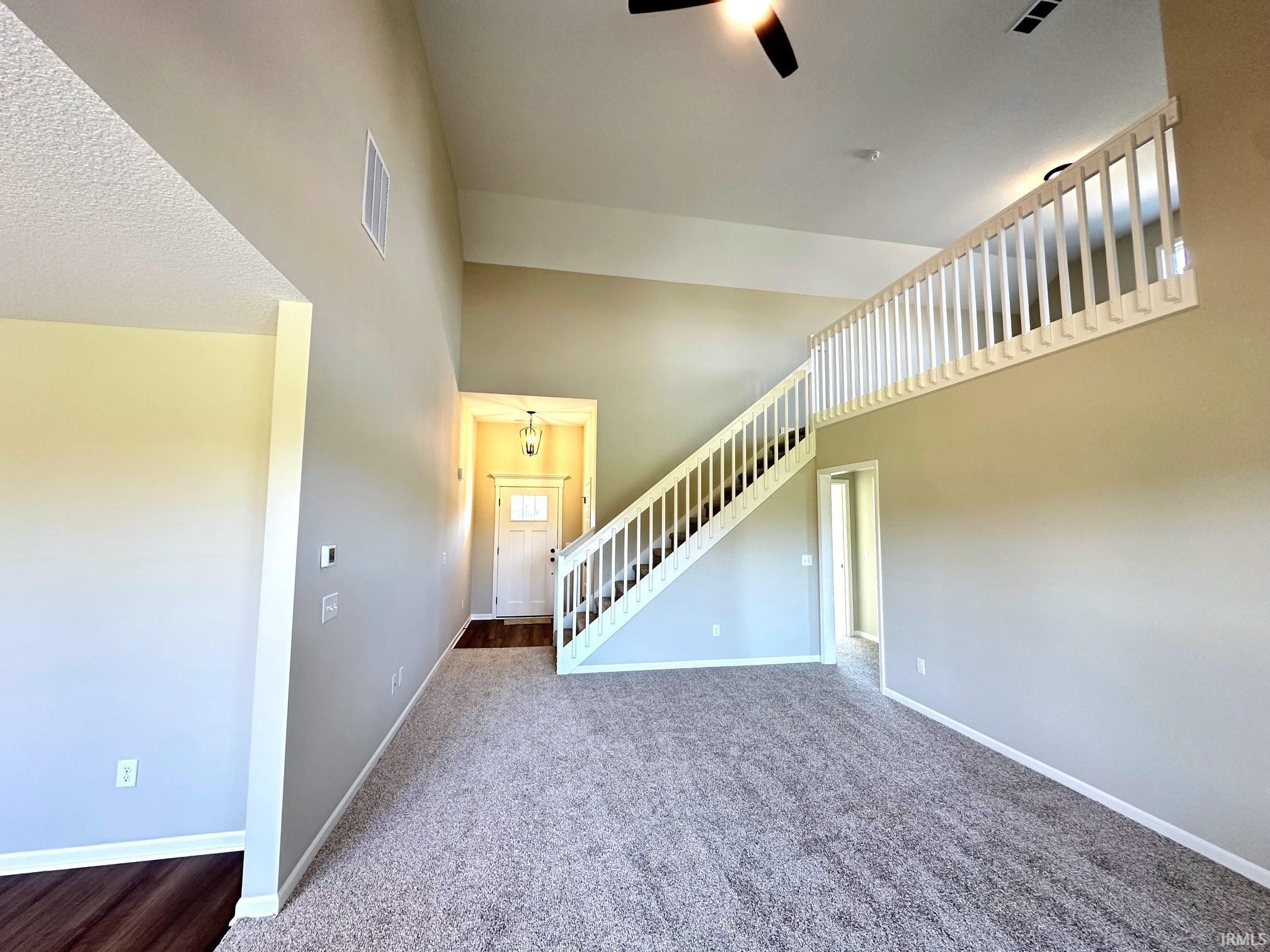 Unfurnished living room featuring dark colored carpet, a high ceiling, and ceiling fan