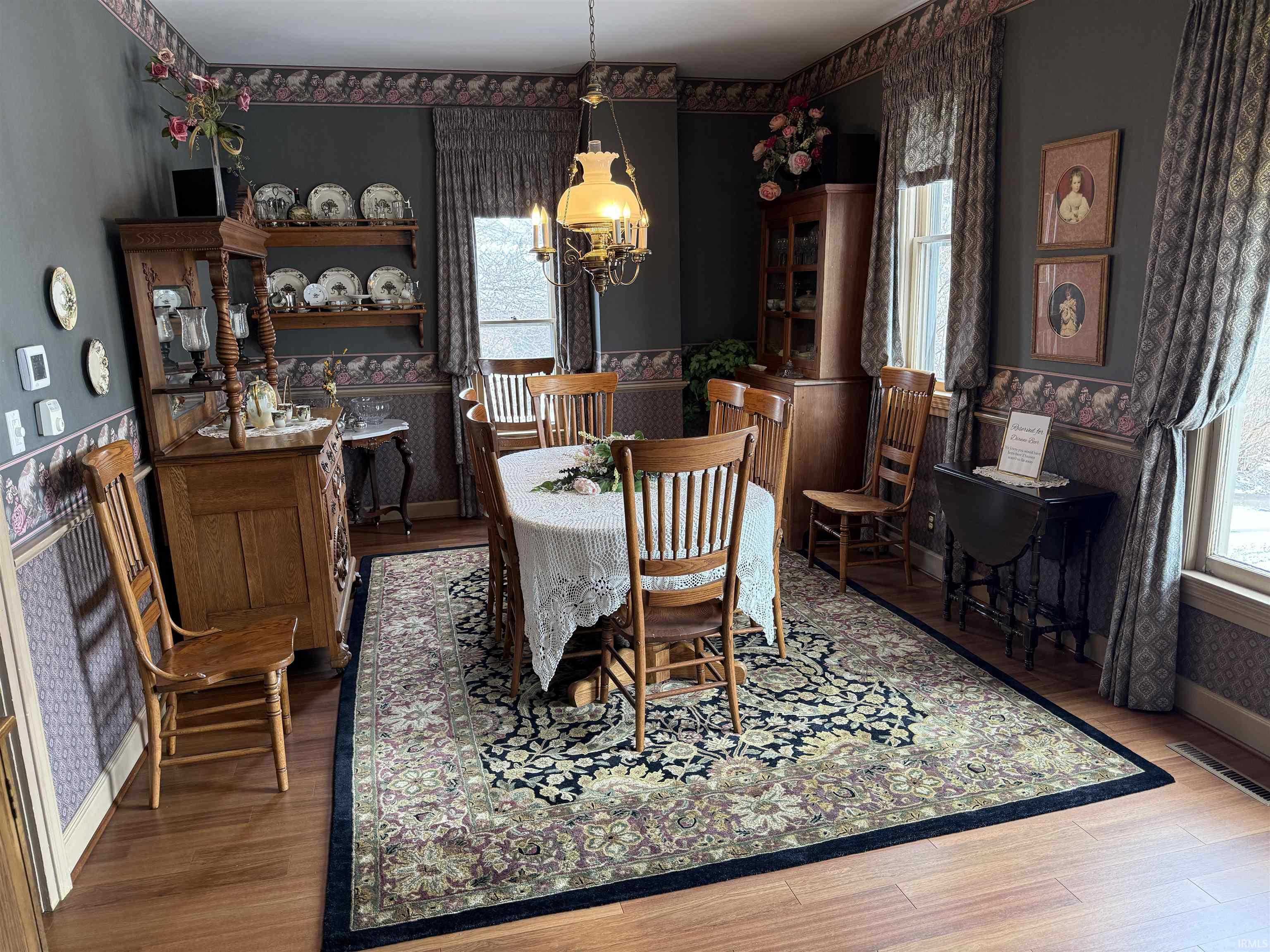 Dining space with wallpapered walls, a wainscoted wall, a chandelier, and wood finished floors