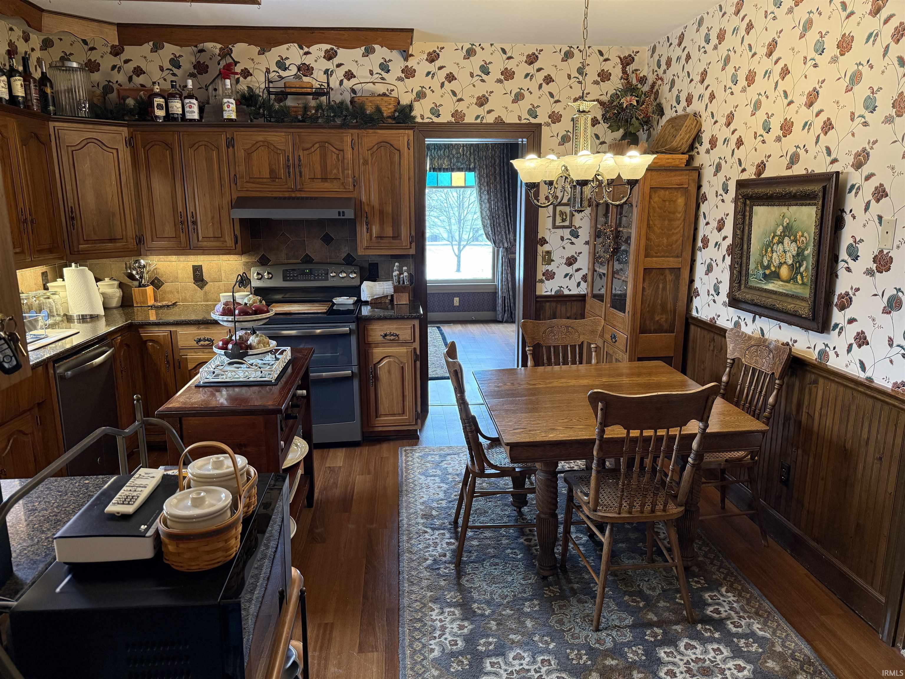 Kitchen with wainscoting, wallpapered walls, stainless steel appliances, a chandelier, and dark wood finished floors