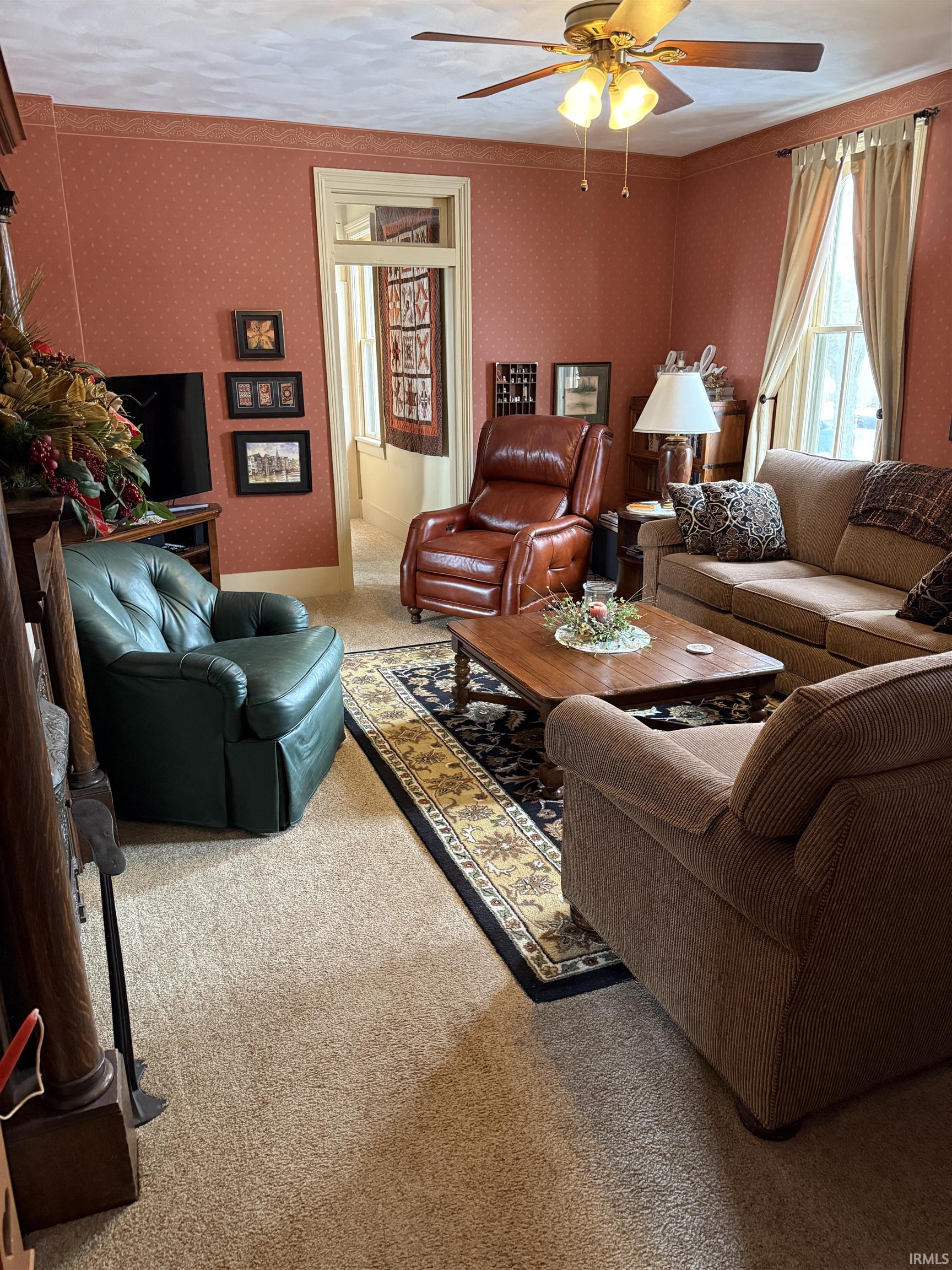 Living room with light colored carpet, wallpapered walls, a ceiling fan, and crown molding