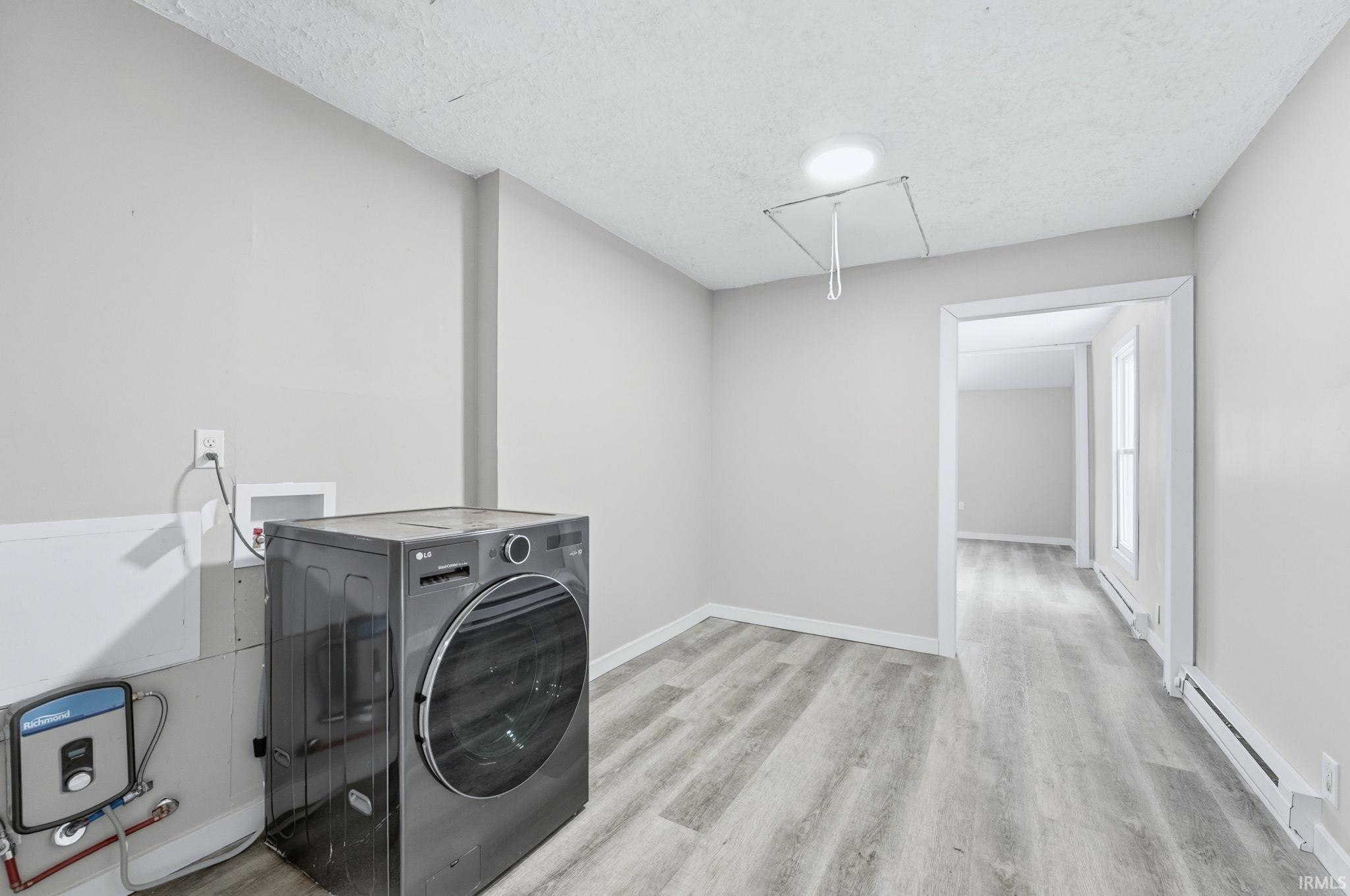 Laundry area featuring washer / dryer, a textured ceiling, baseboard heating, attic access, and light wood-type flooring