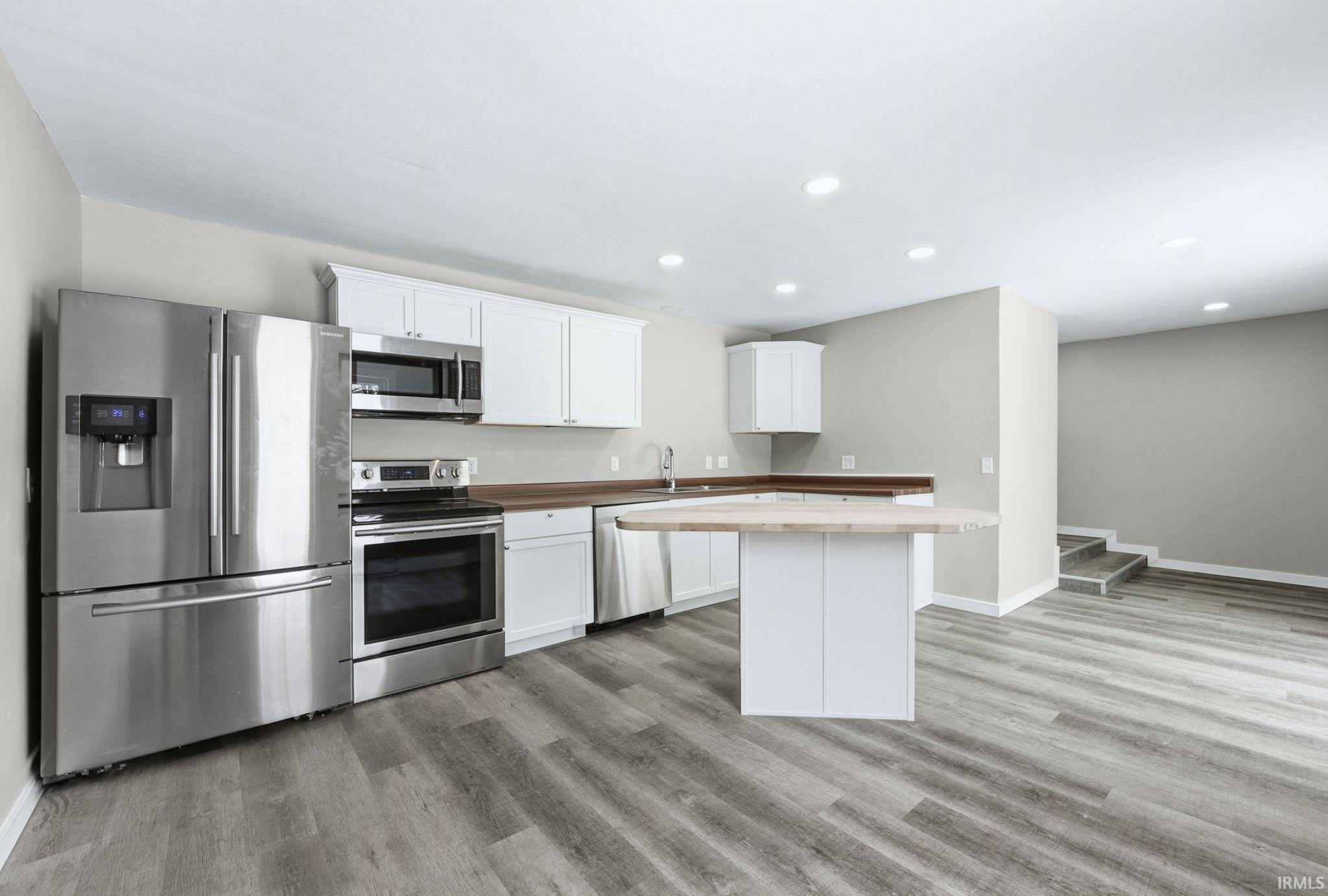 Kitchen with stainless steel appliances, white cabinets, butcher block countertops, recessed lighting, and a kitchen island