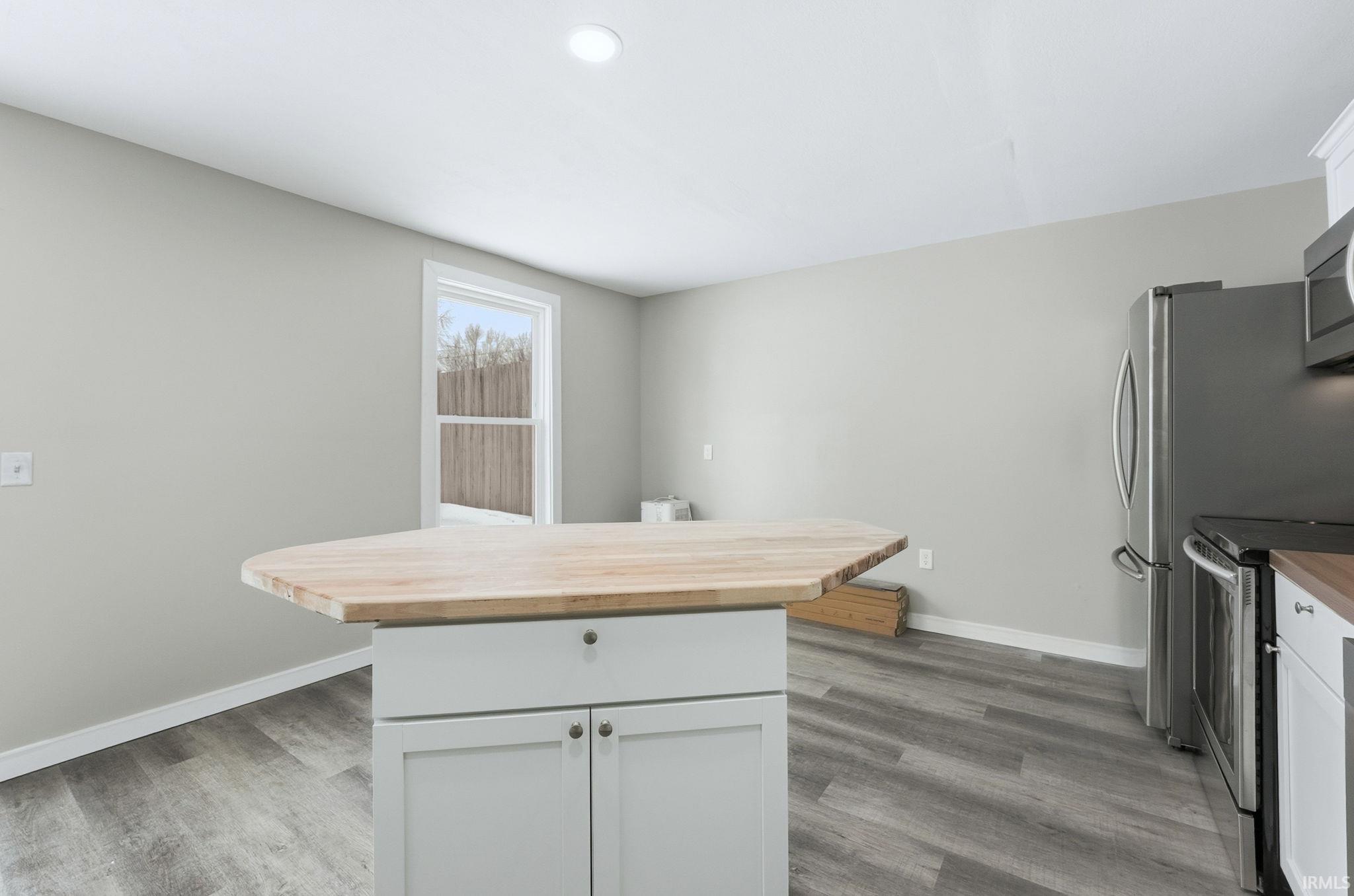 Kitchen featuring wooden counters, stainless steel appliances, white cabinetry, a center island, and dark wood-style flooring