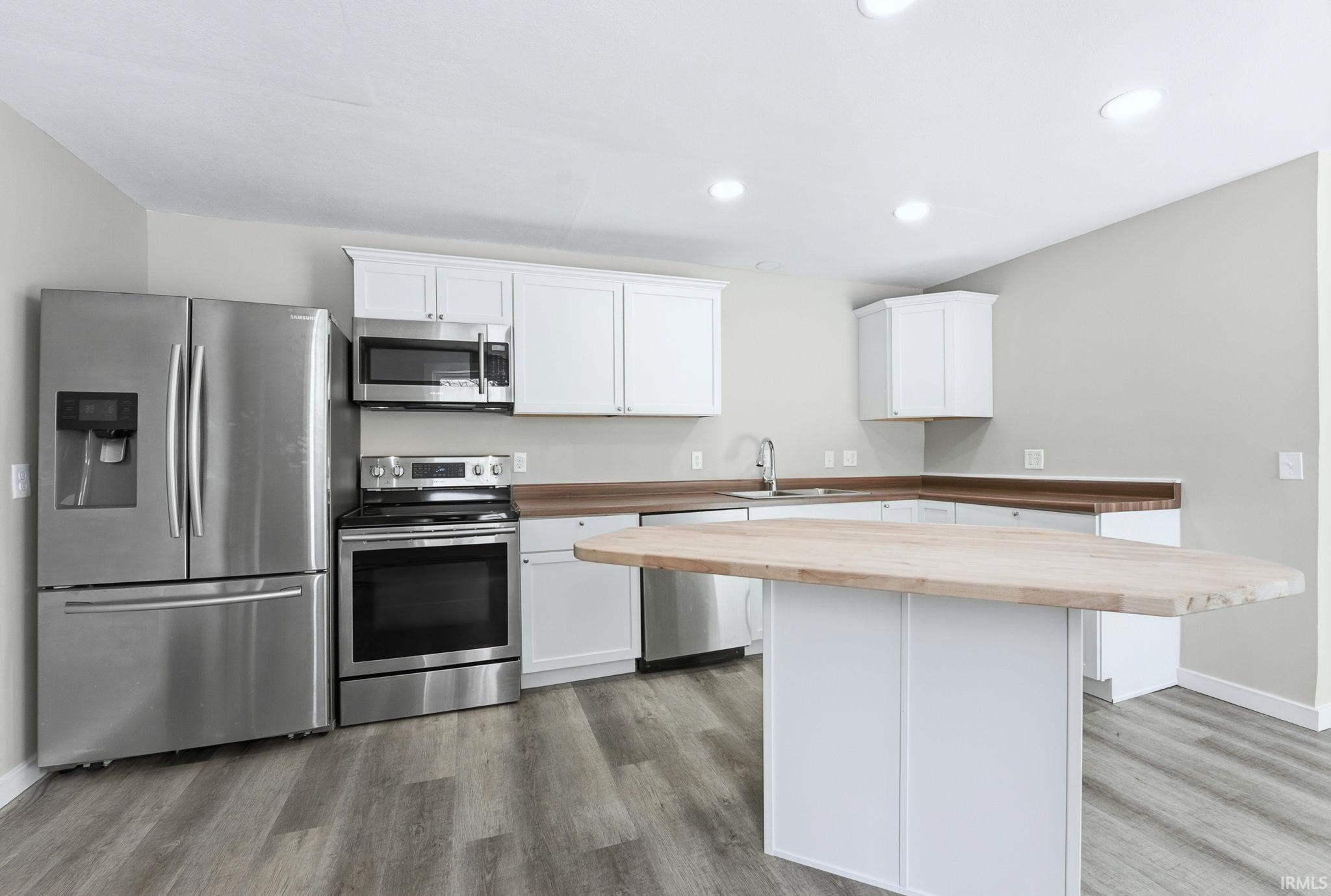 Kitchen with appliances with stainless steel finishes, white cabinetry, wood counters, light wood-style flooring, and recessed lighting