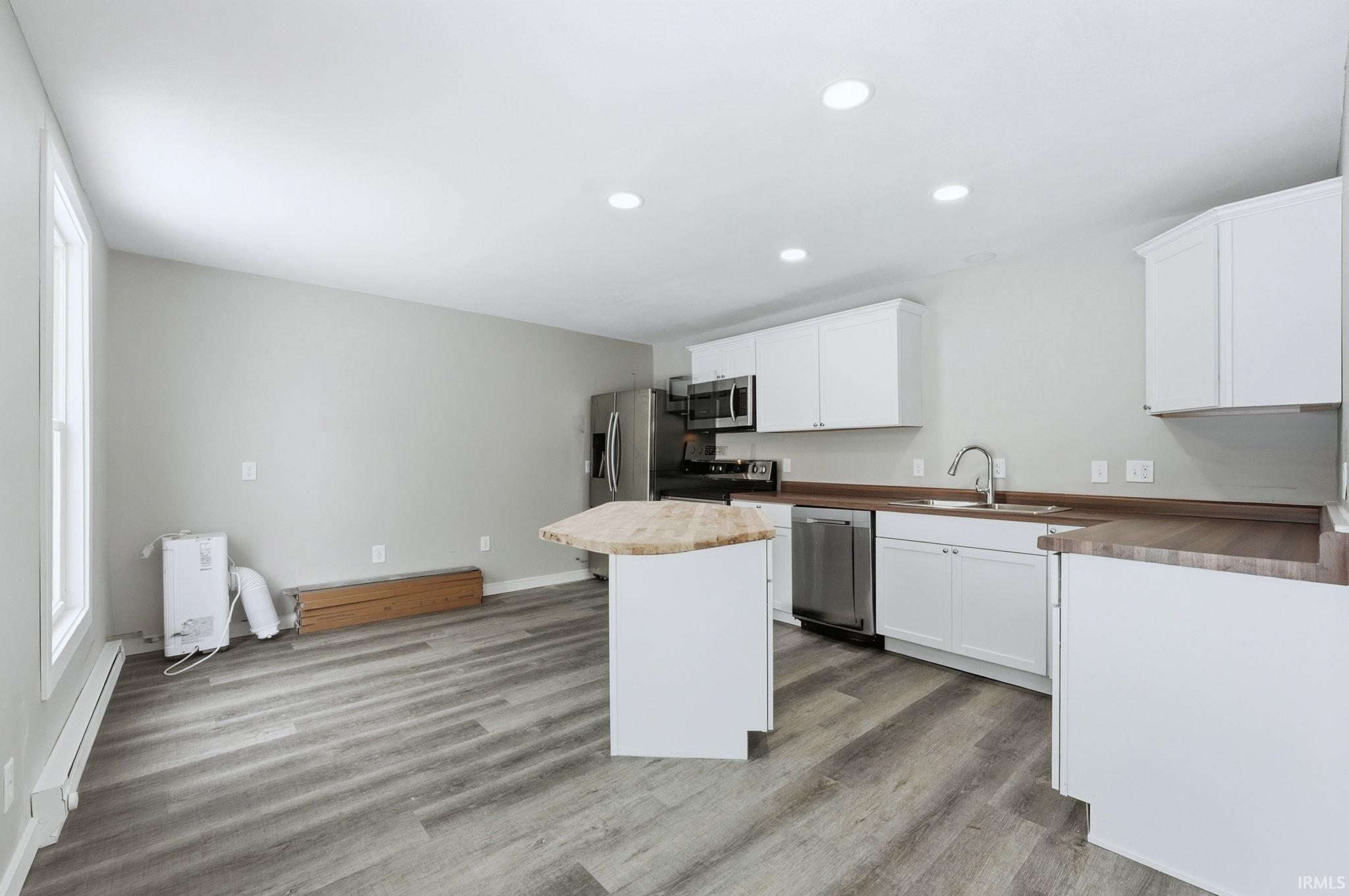 Kitchen featuring white cabinetry, a baseboard radiator, stainless steel appliances, light wood-style flooring, and a kitchen island
