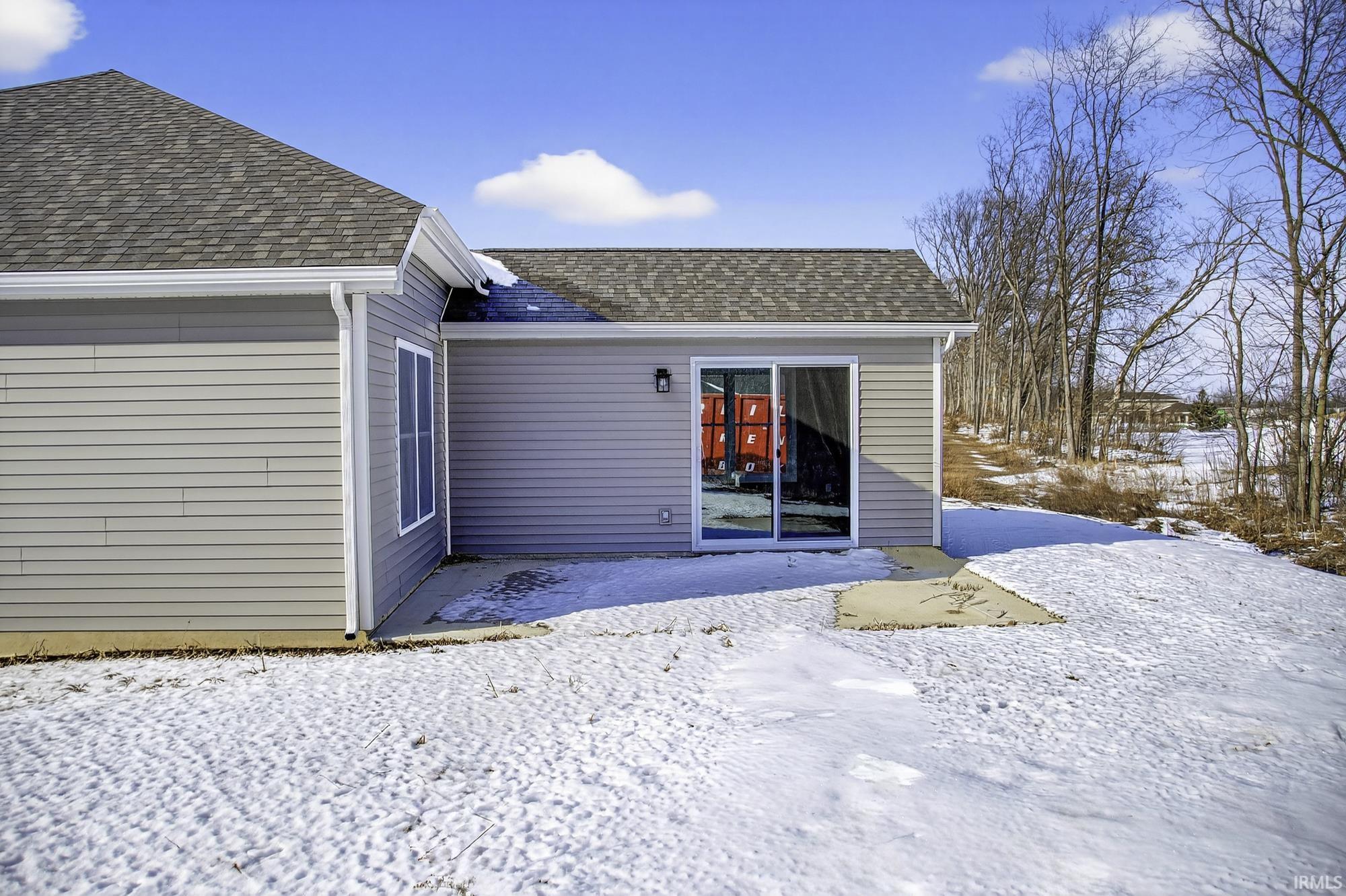 Snow covered back of property featuring a patio and a shingled roof