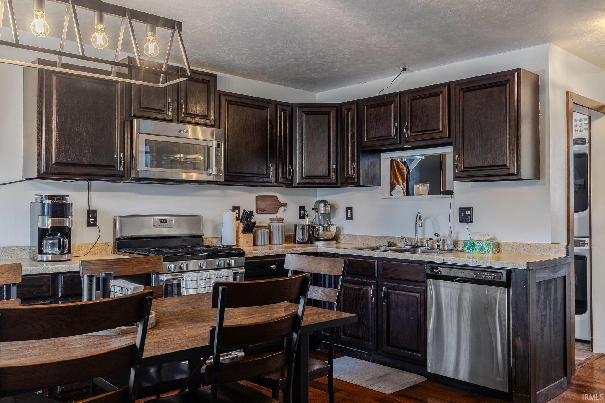 Kitchen with dark wood finish cabinets, light countertops, stainless steel appliances, dark wood finished floors, and stacked washer and dryer