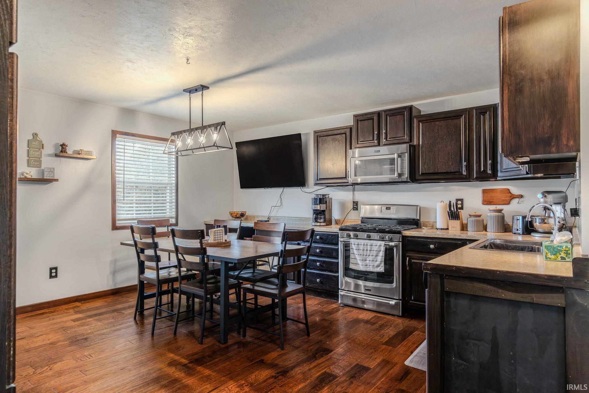 Kitchen featuring stainless steel appliances, dark wood finish cabinetry, light countertops, pendant lighting, and dark wood-style flooring