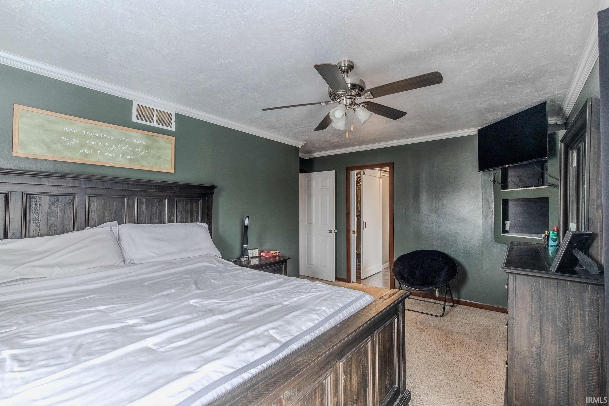 Bedroom featuring a ceiling fan, crown molding, dark aggregate flooring, and a textured ceiling