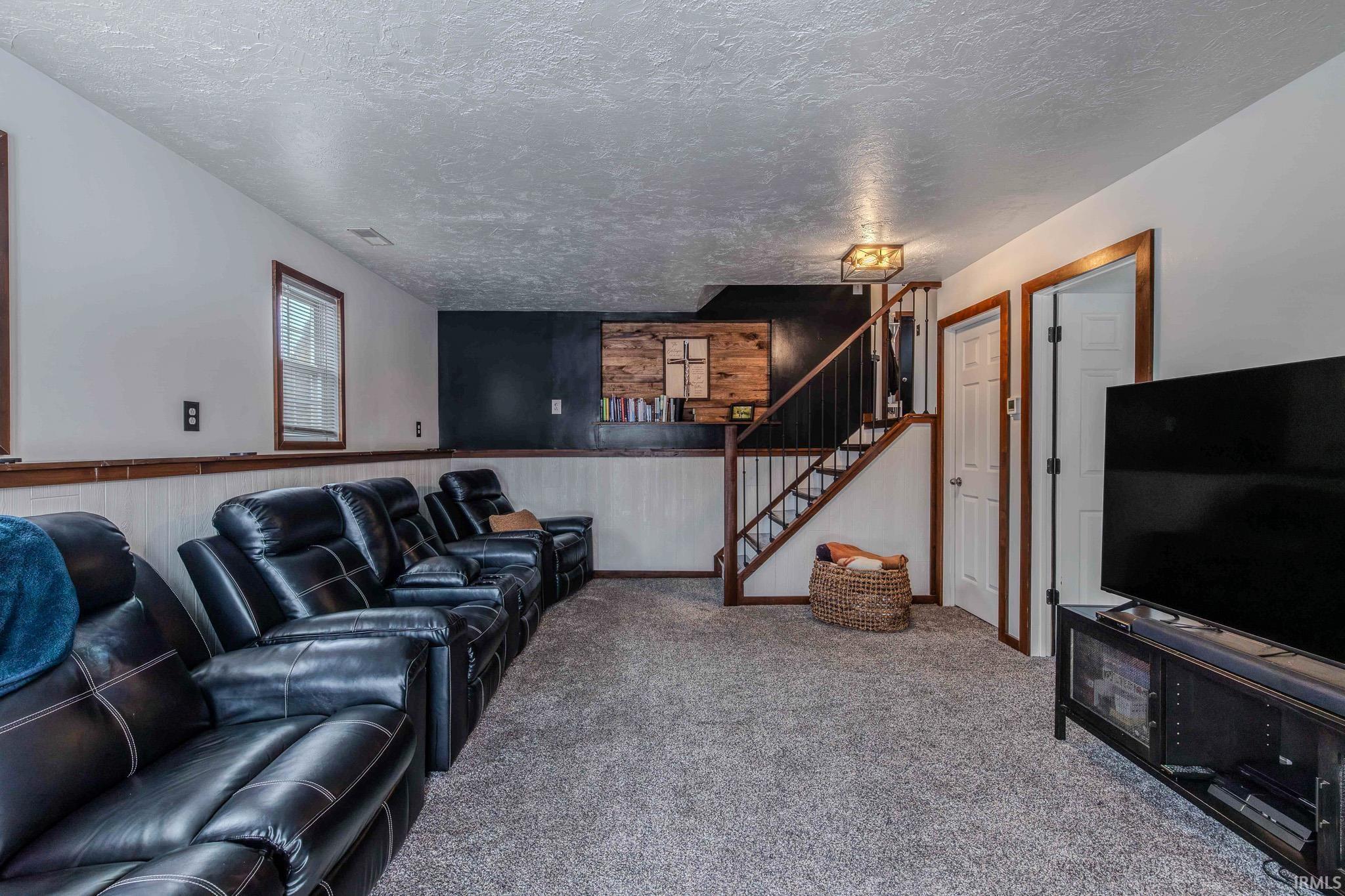 Living room featuring wooden walls, carpet, a textured ceiling, and wainscoting
