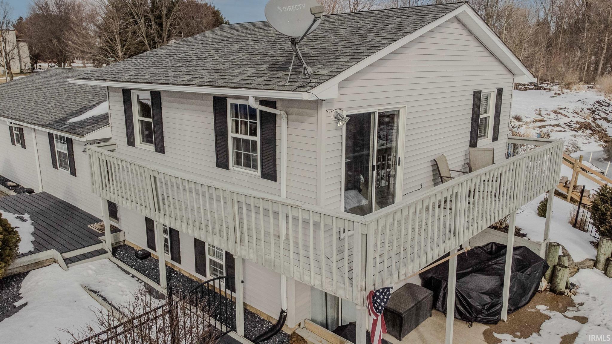 View of snowy exterior with a deck and a shingled roof