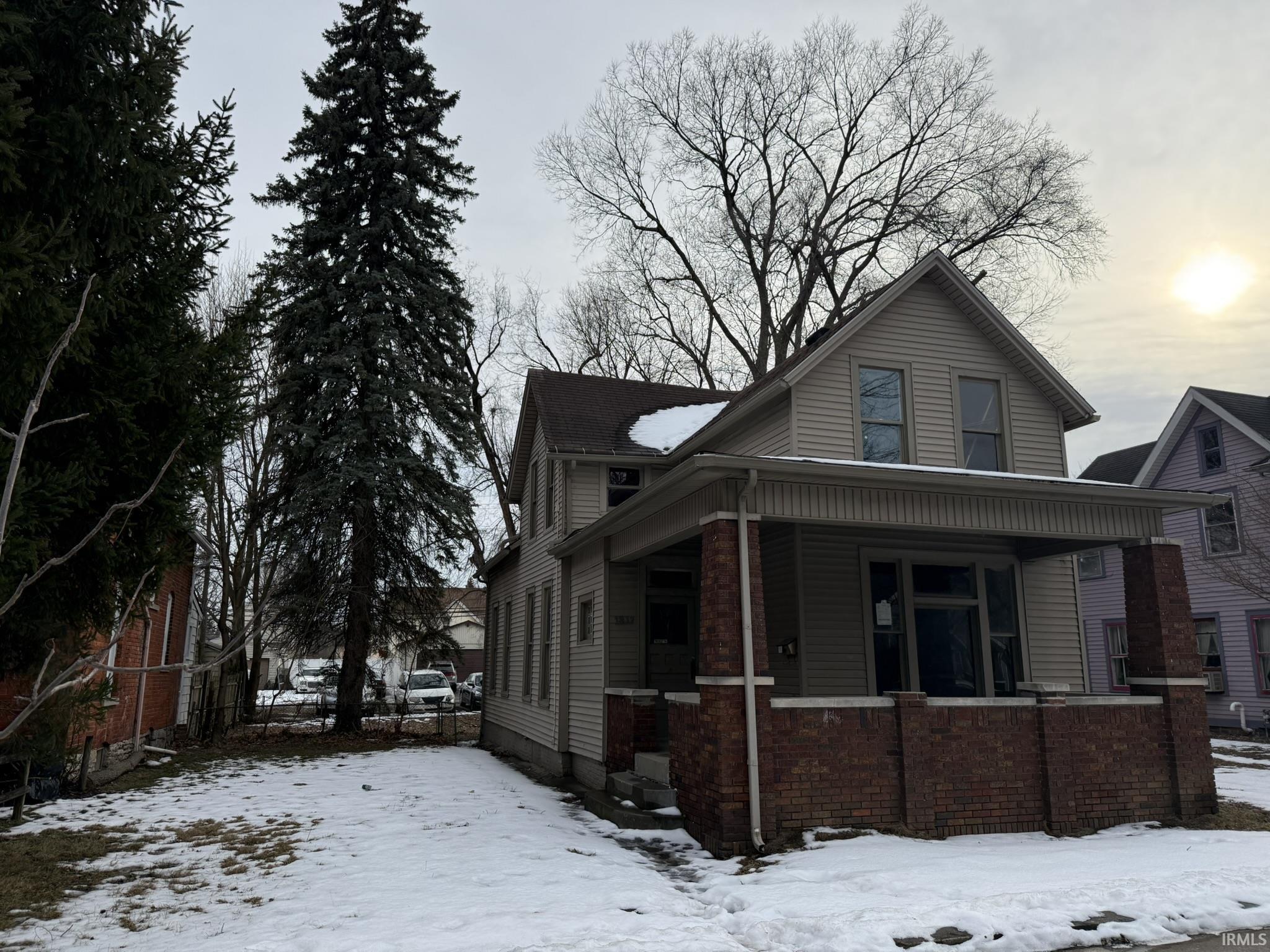 View of snowy exterior with brick siding and covered porch
