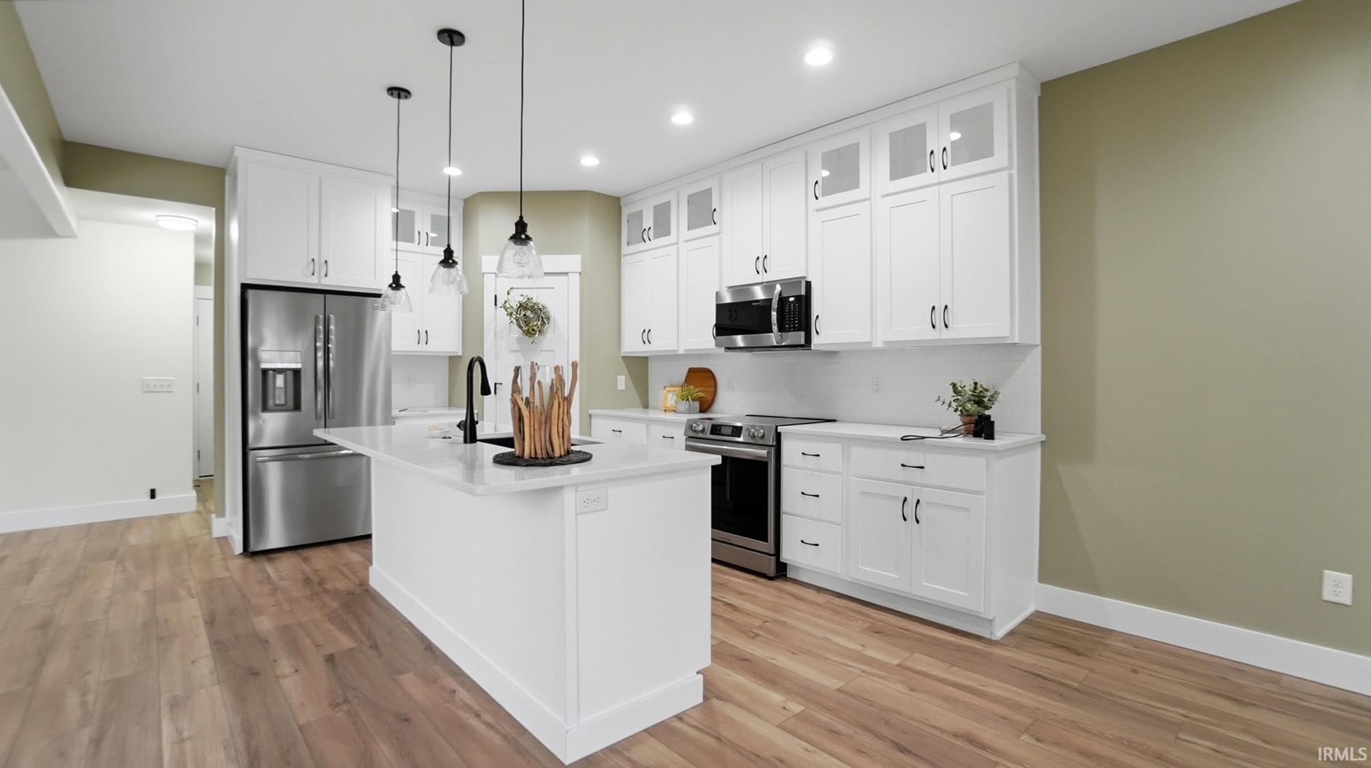 Kitchen with stainless steel appliances, a kitchen island with sink, decorative light fixtures, white cabinetry, and light wood finished floors