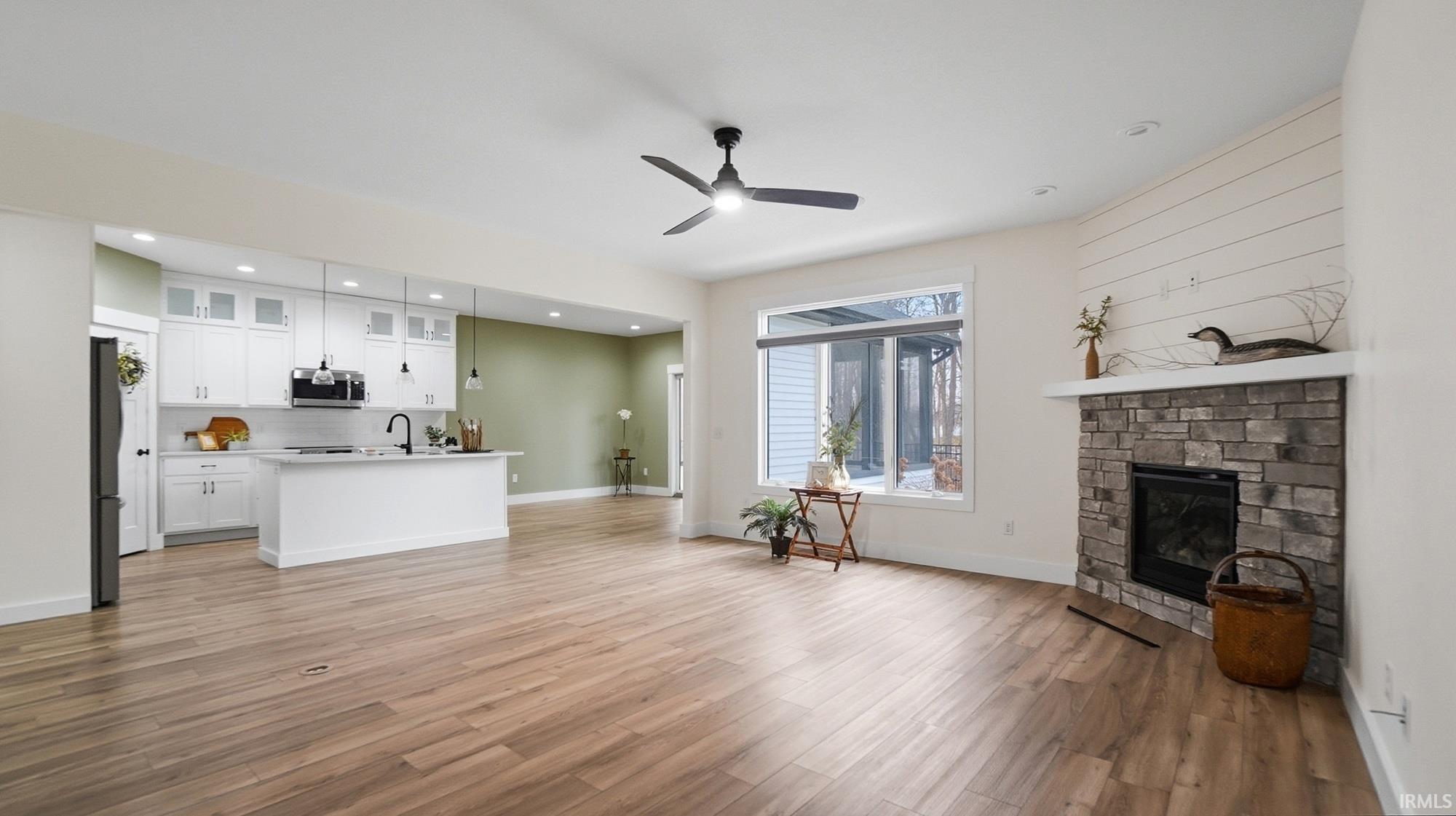 Living area with a stone fireplace, a ceiling fan, light wood-type flooring, and recessed lighting