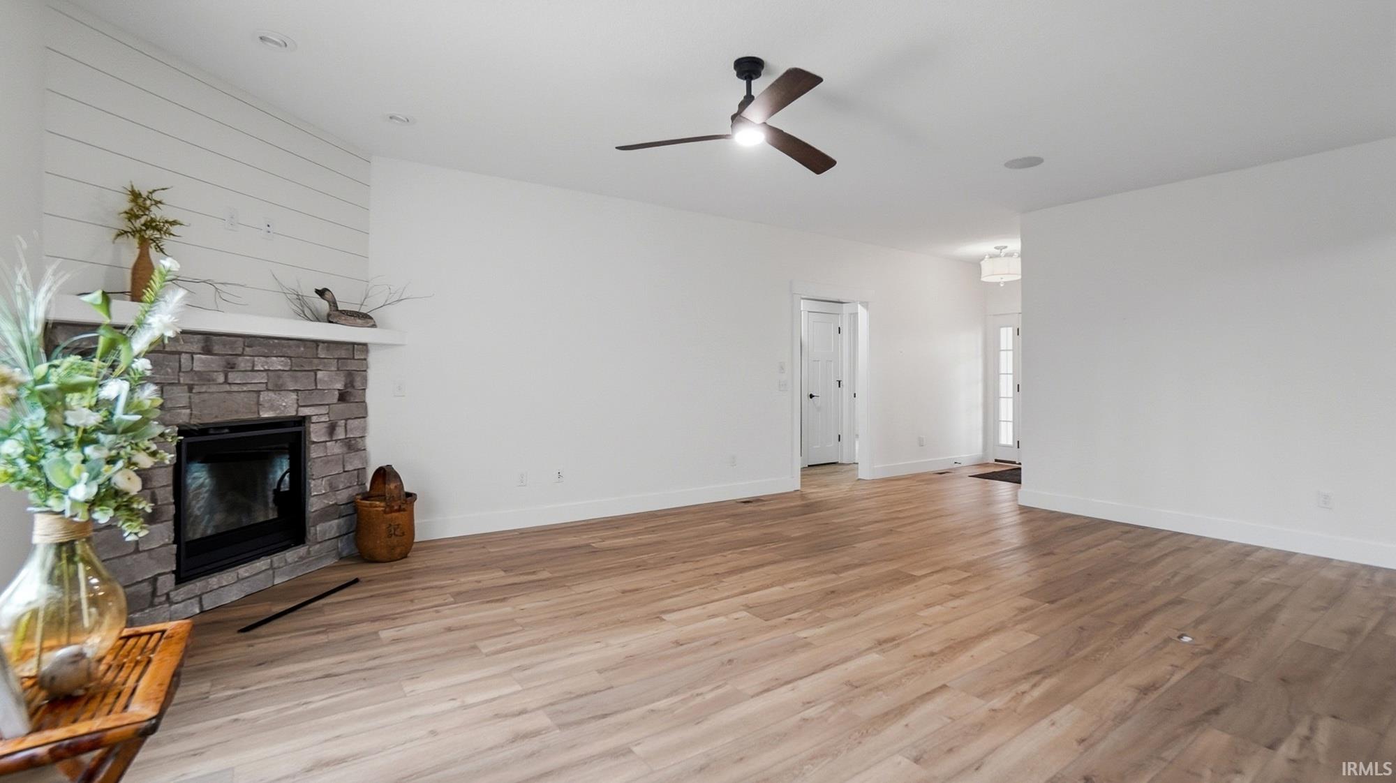 Unfurnished living room featuring a fireplace, a ceiling fan, and light wood finished floors