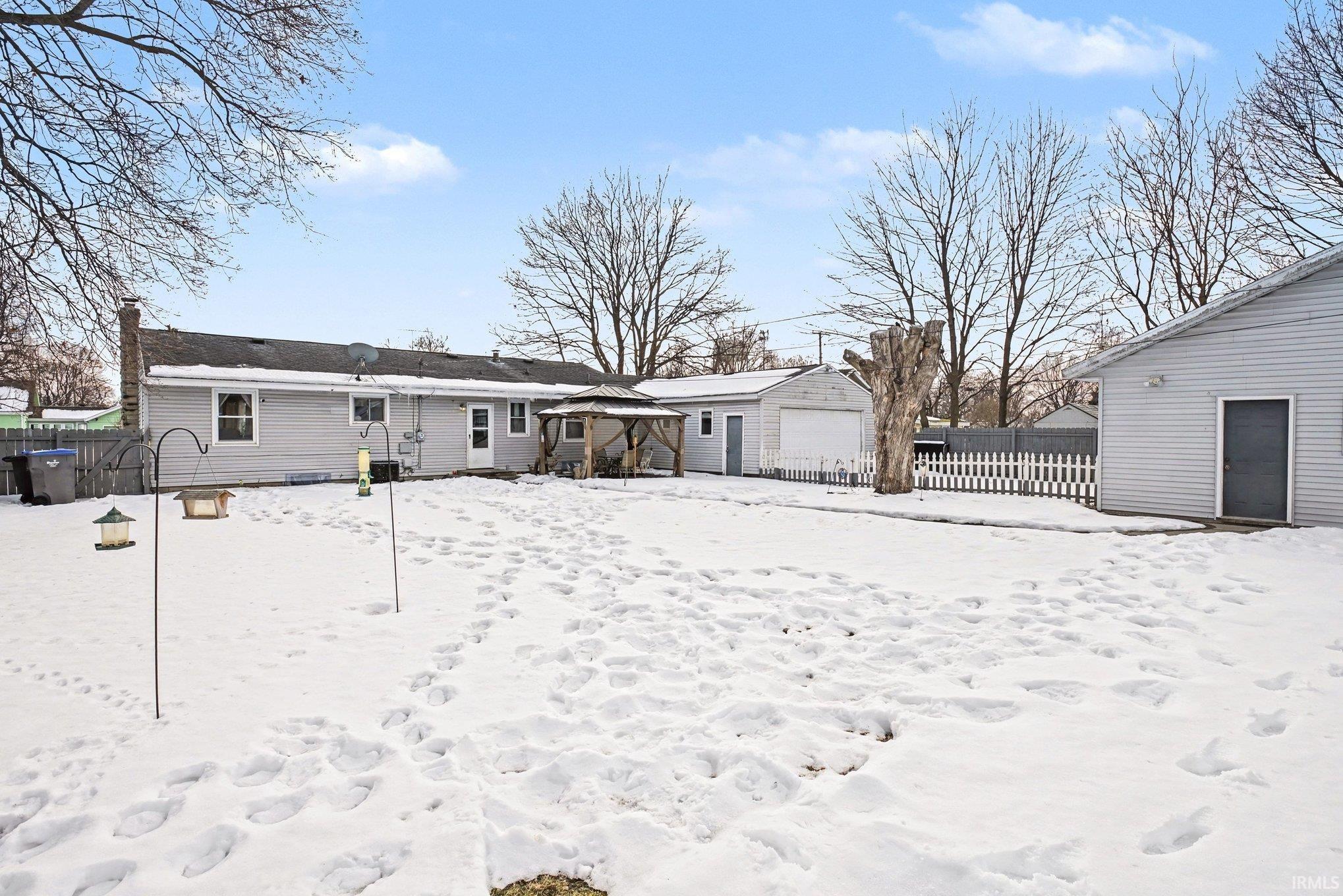 Snow covered back of property featuring an outbuilding, a chimney, a gazebo, and a garage