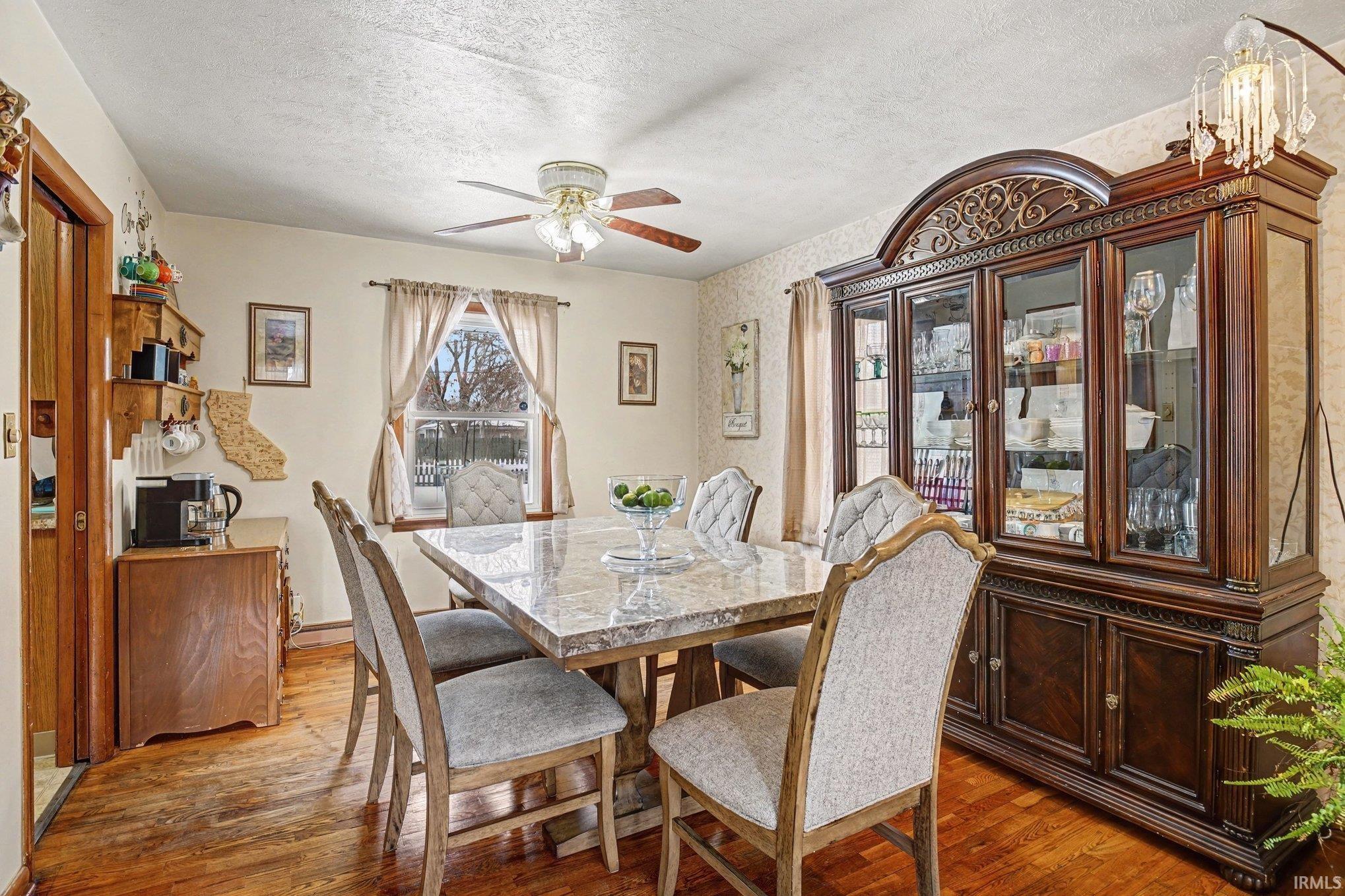 Dining room featuring hardwood / wood-style floors, a ceiling fan, a textured ceiling, and wallpapered walls