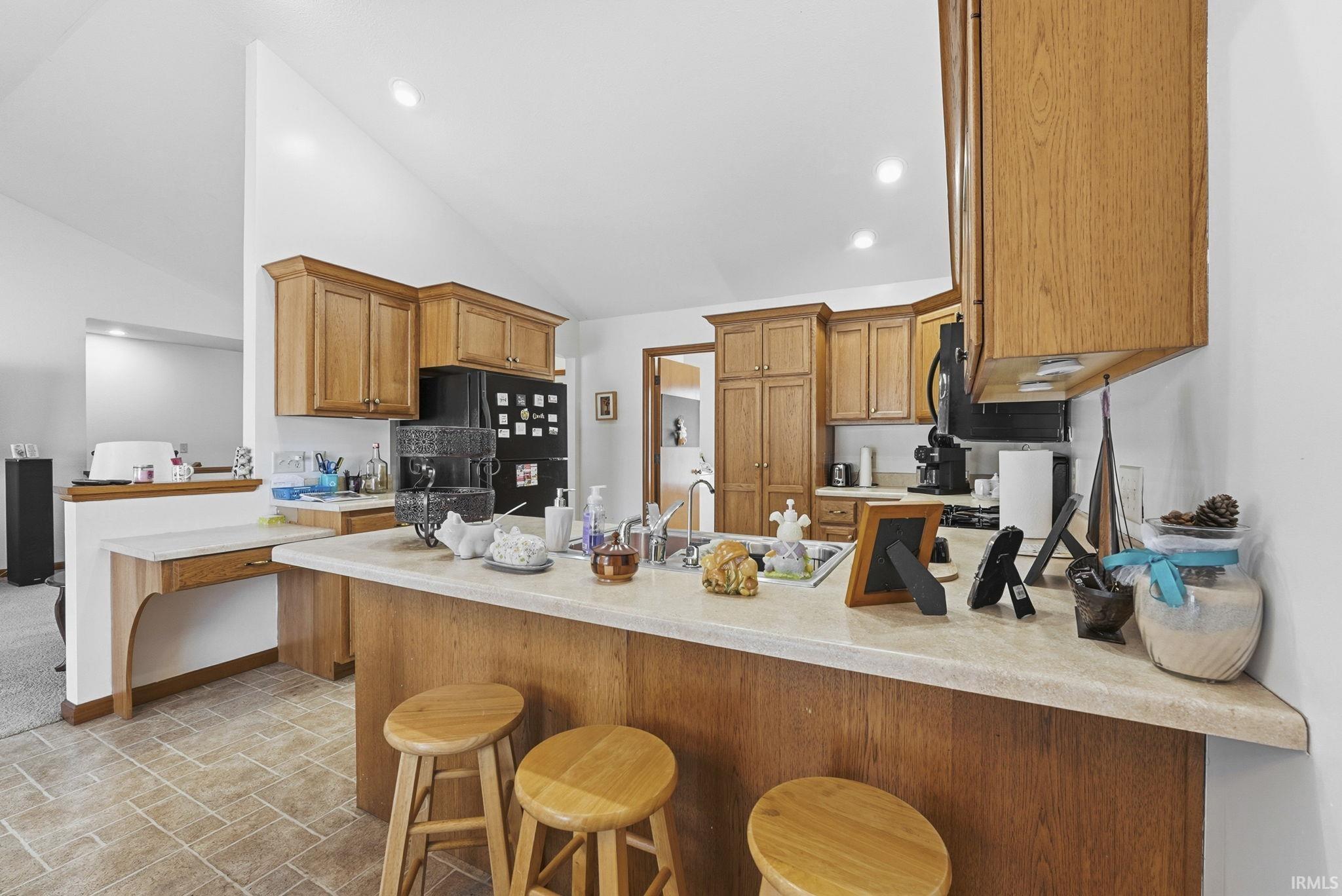 Kitchen with a peninsula, wood finish cabinets, a breakfast bar area, freestanding refrigerator, and recessed lighting
