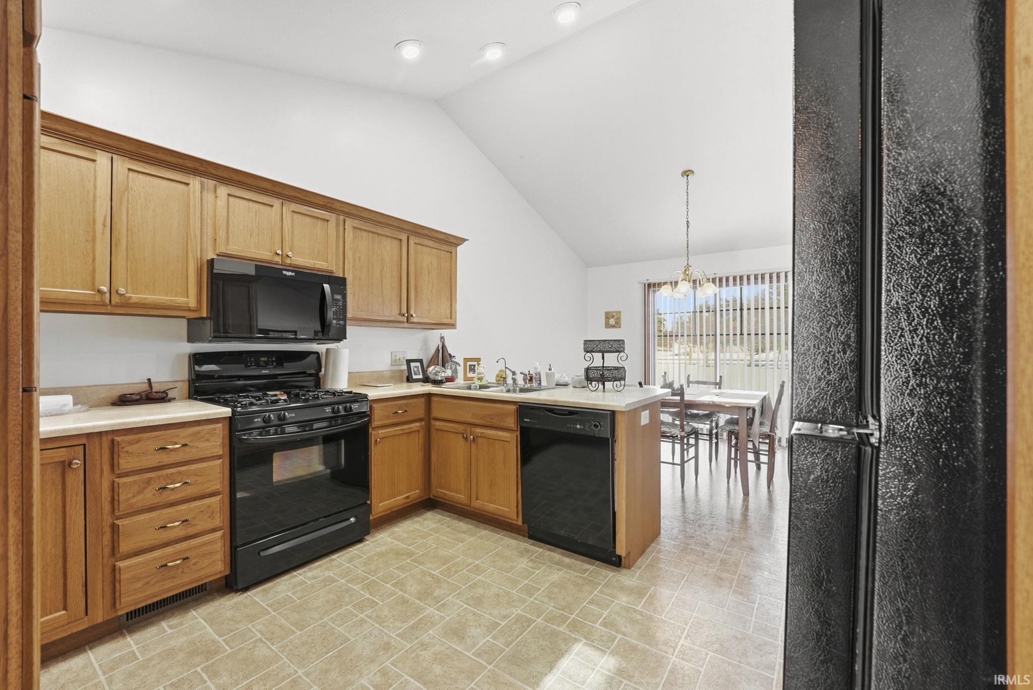 Kitchen with black appliances, light countertops, a peninsula, lofted ceiling, and hanging lights