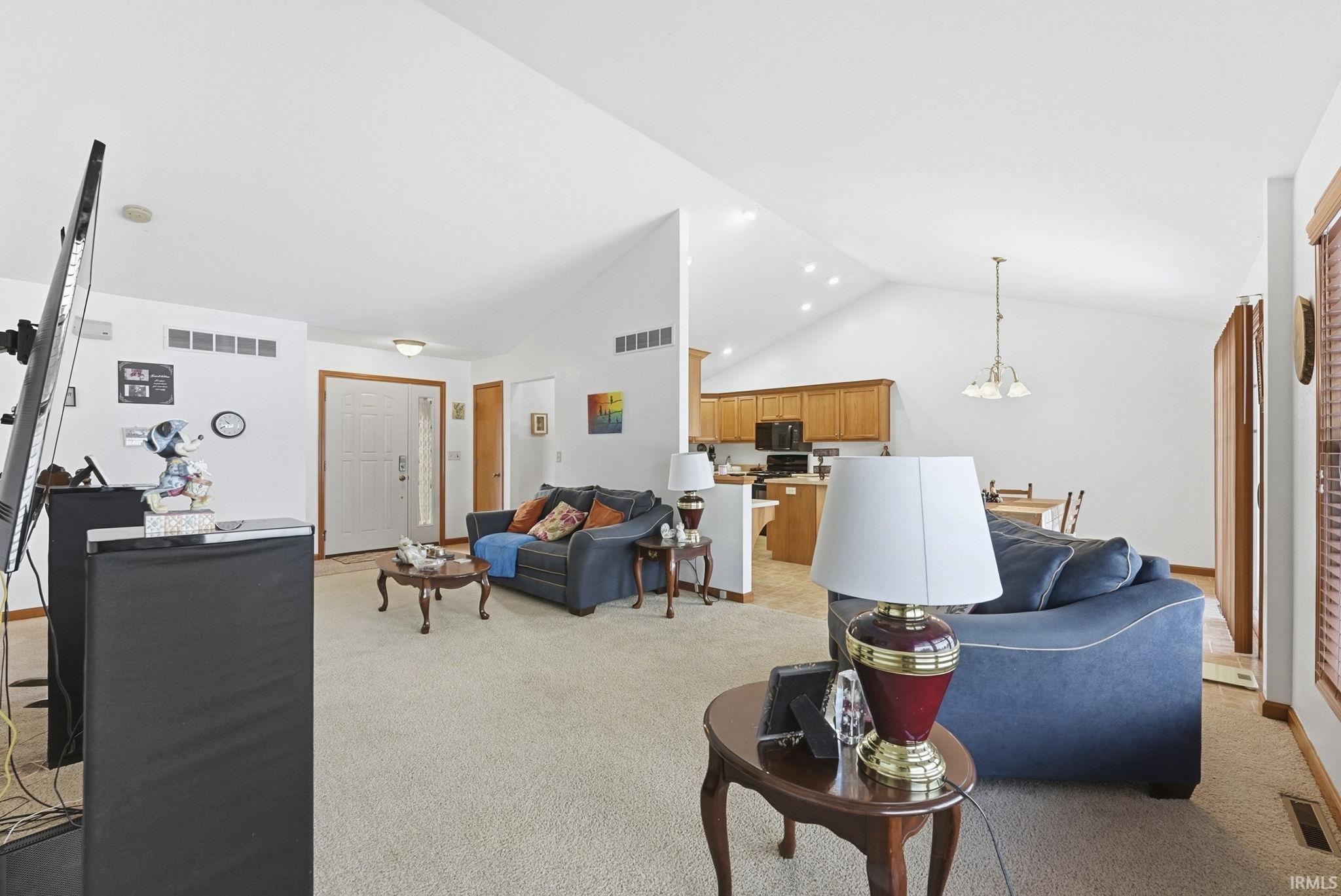 Living area featuring light colored carpet, hanging lights, and a high ceiling
