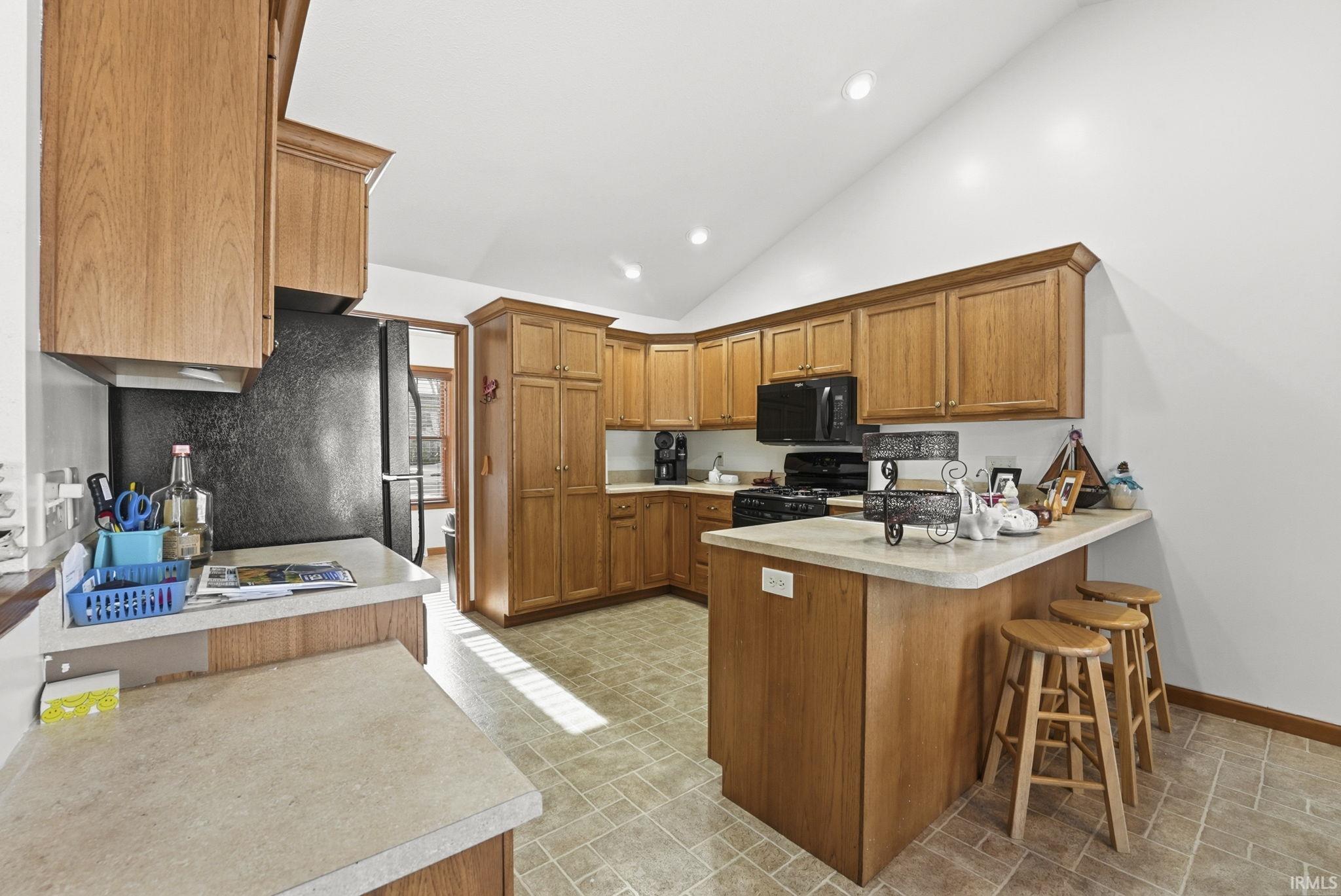 Kitchen with wood finish cabinetry, a peninsula, light countertops, black appliances, and vaulted ceiling