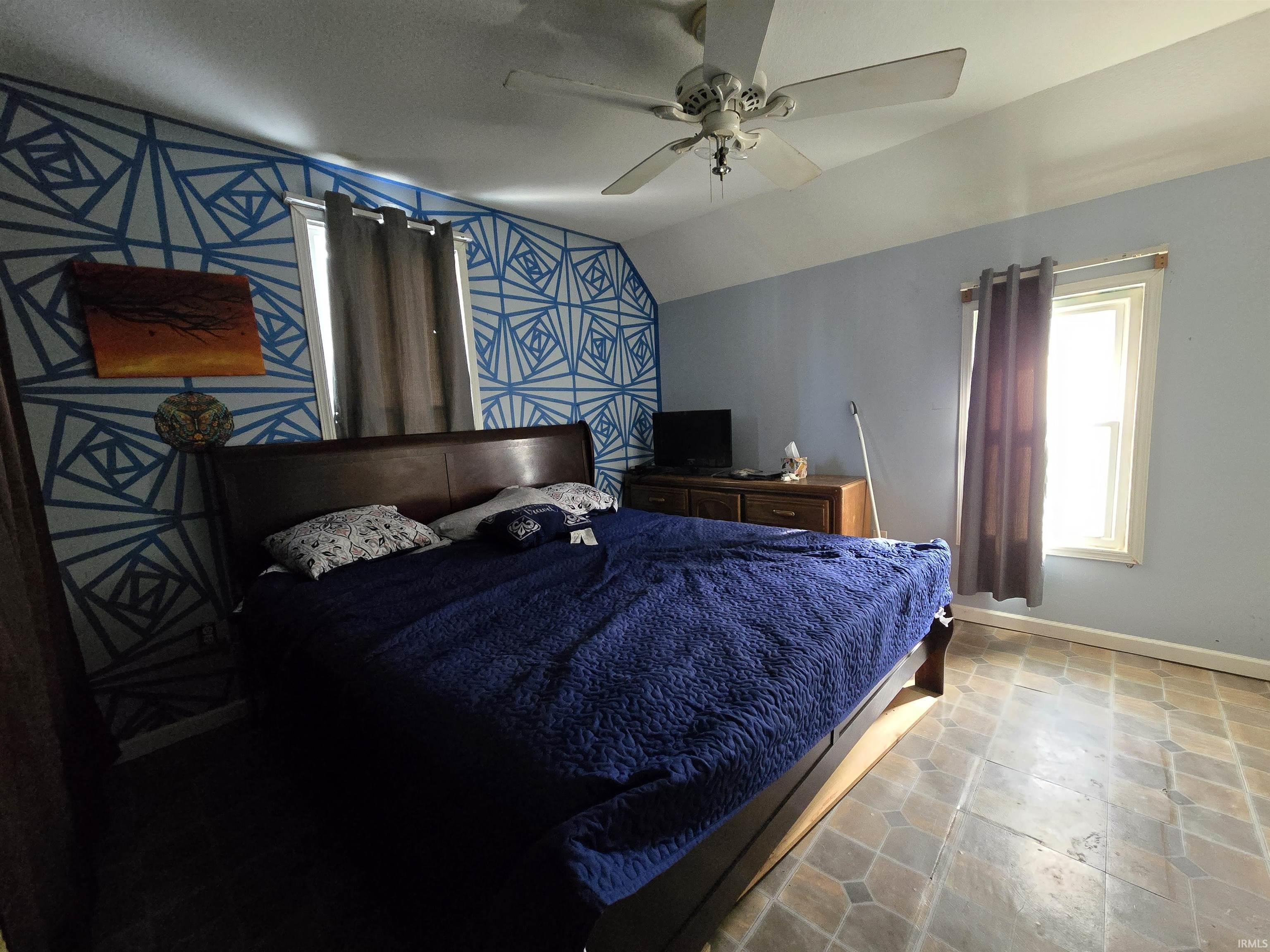Bedroom featuring a ceiling fan, lofted ceiling, and an accent wall