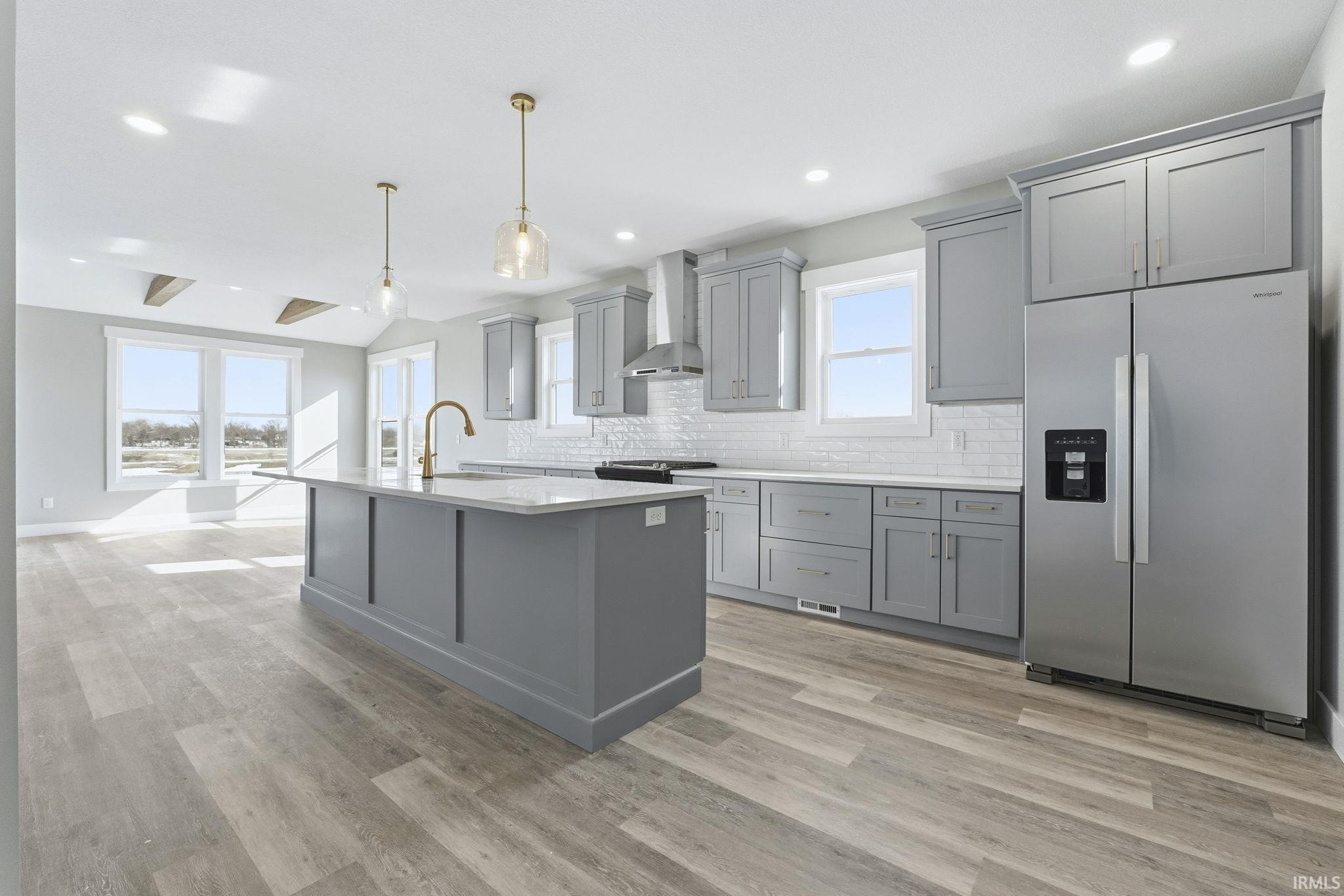 Kitchen with stainless steel appliances, gray cabinetry, hanging light fixtures, an island with sink, and vaulted ceiling