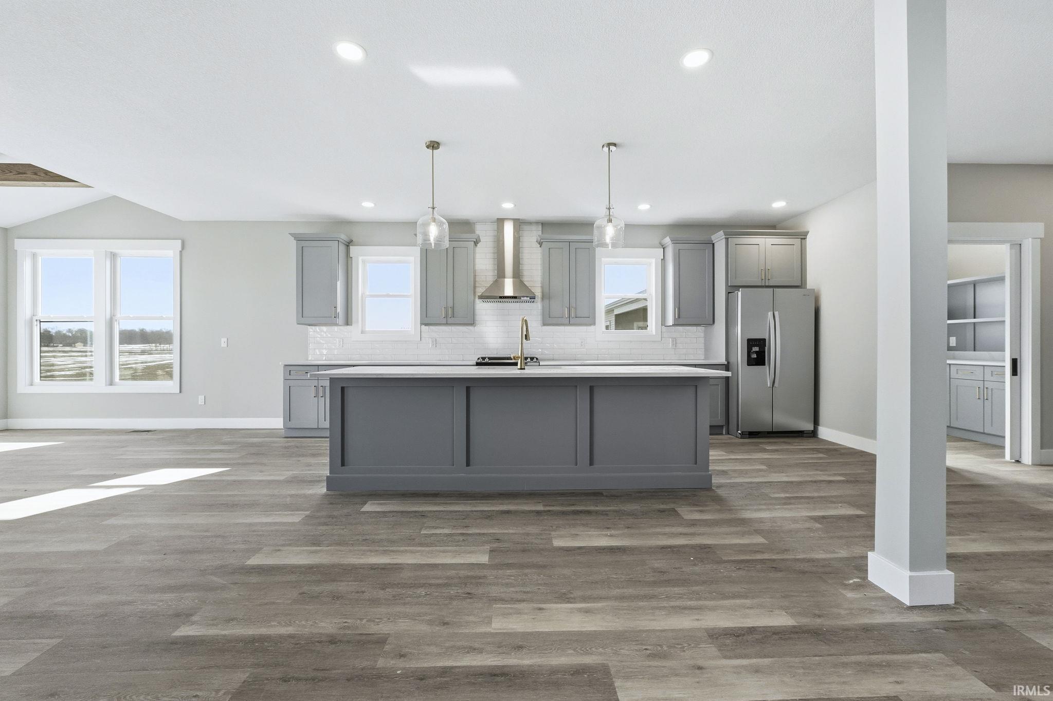Kitchen with gray cabinetry, pendant lighting, stainless steel refrigerator with ice dispenser, an island with sink, and light wood-style flooring