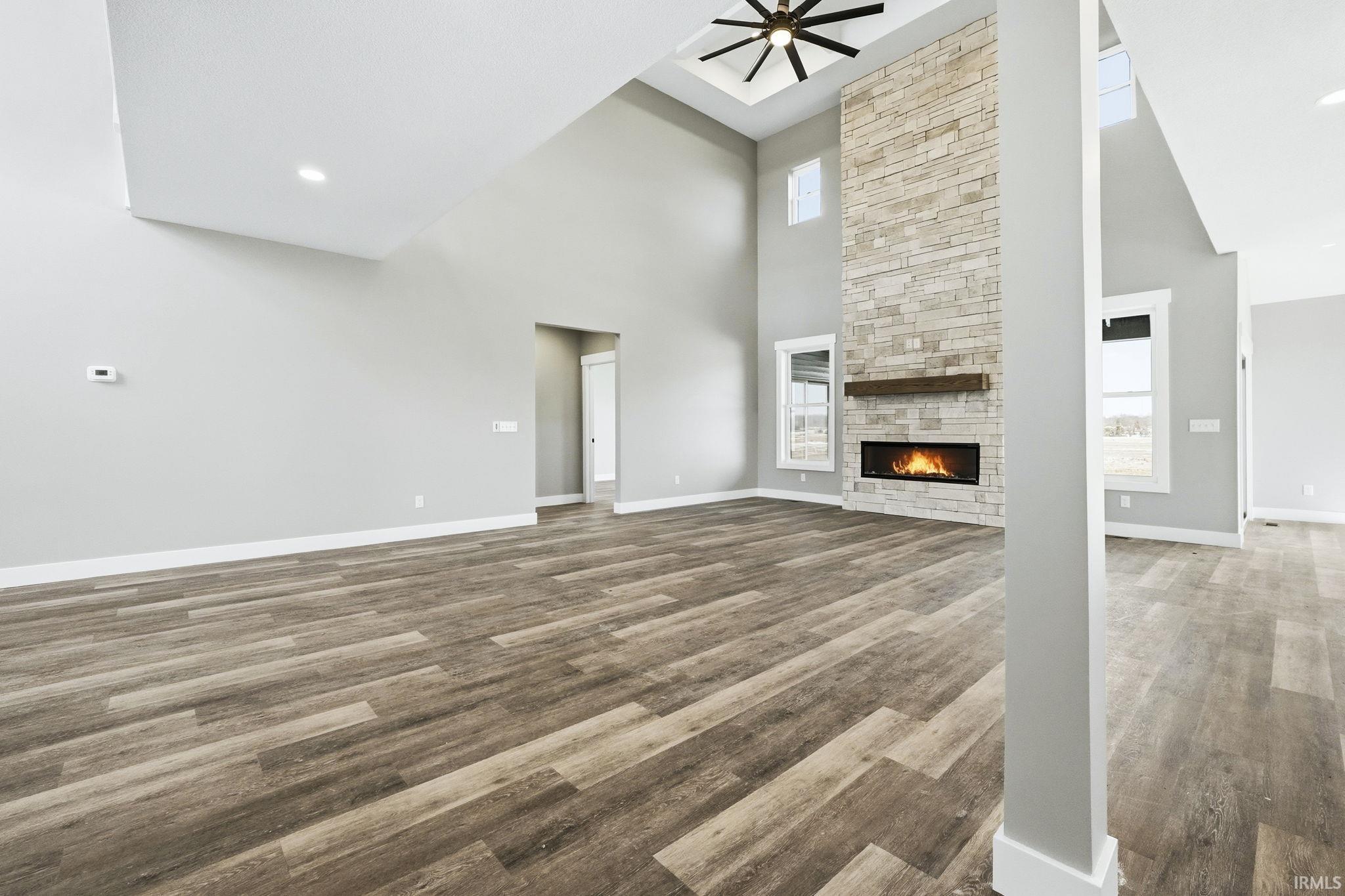 Unfurnished living room with a stone fireplace, a high ceiling, wood finished floors, ceiling fan, and recessed lighting