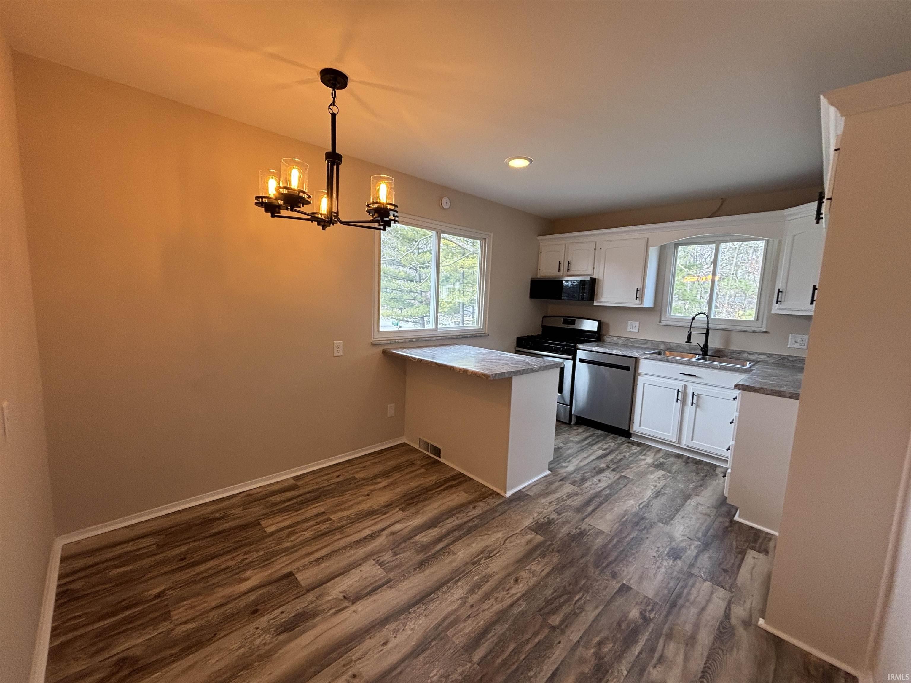 Kitchen featuring white cabinetry, stainless steel appliances, dark wood-type flooring, suspended lighting, and a peninsula