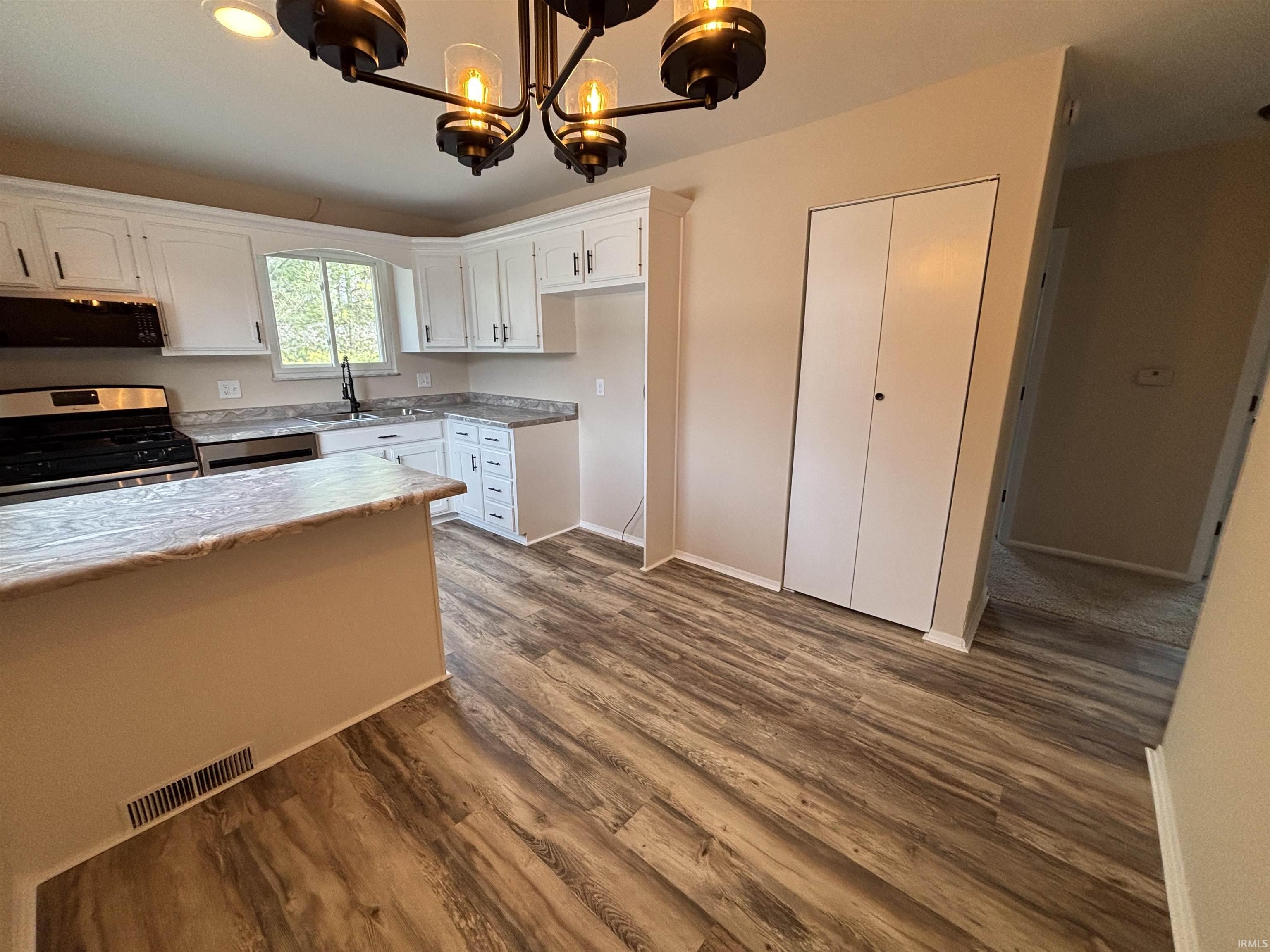 Kitchen featuring white cabinets, stainless steel appliances, hanging lights, dark wood finished floors, and exhaust hood
