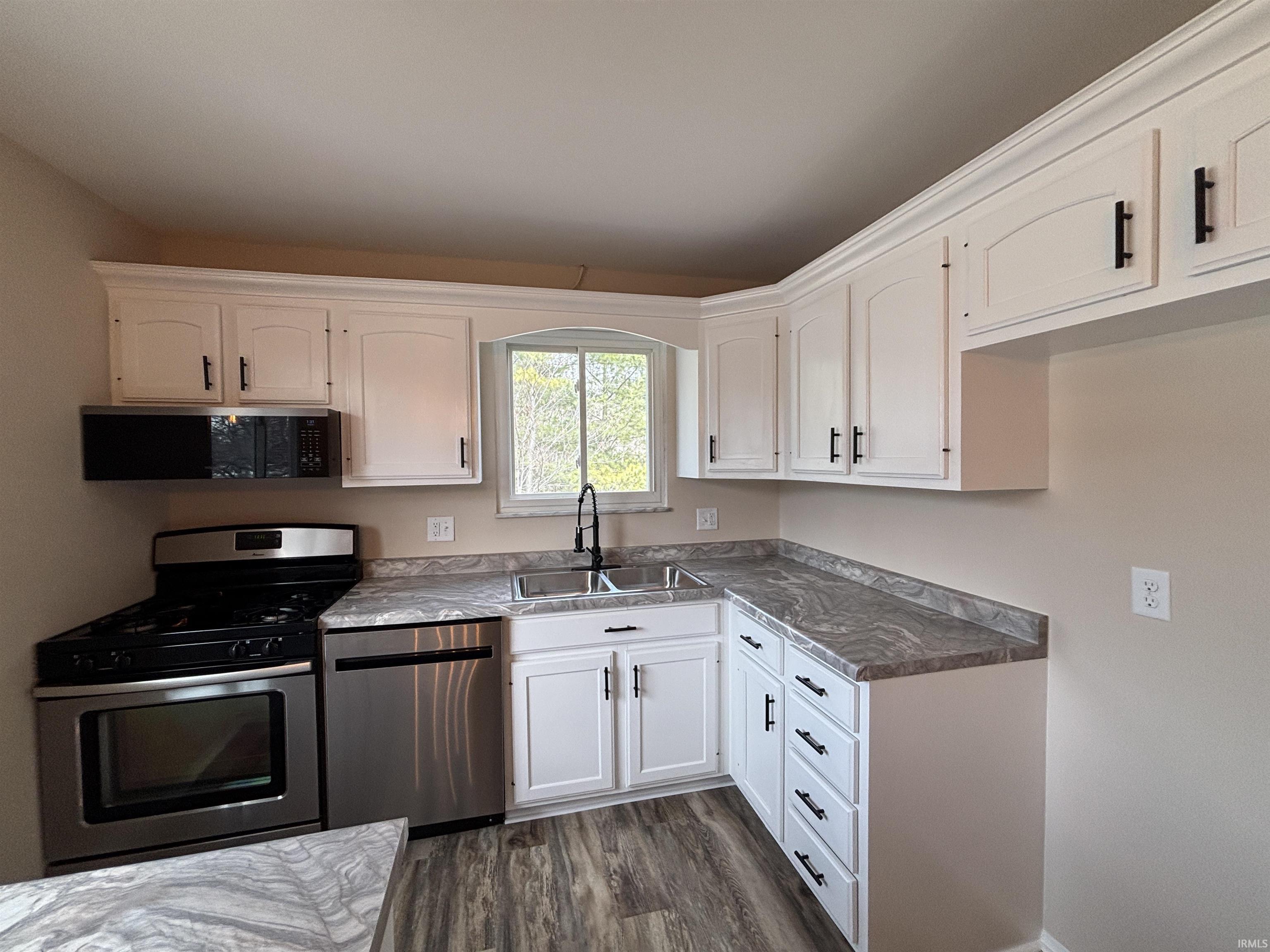 Kitchen with stainless steel appliances, white cabinetry, dark wood-type flooring, and dark countertops