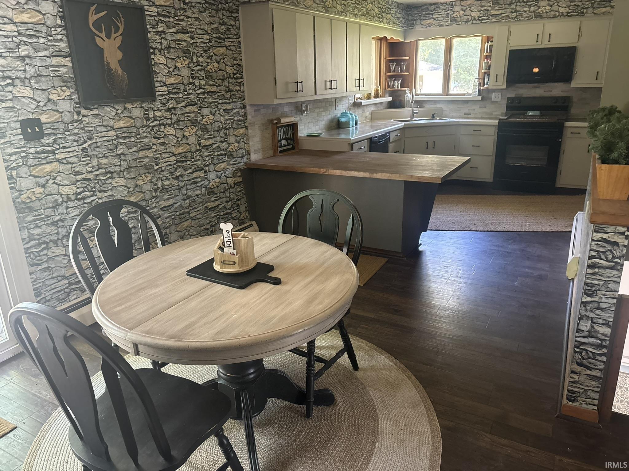 Spacious kitchen with wood-finish flooring, light grey cabinetry, black built-in appliances, and a central island with a wood countertop