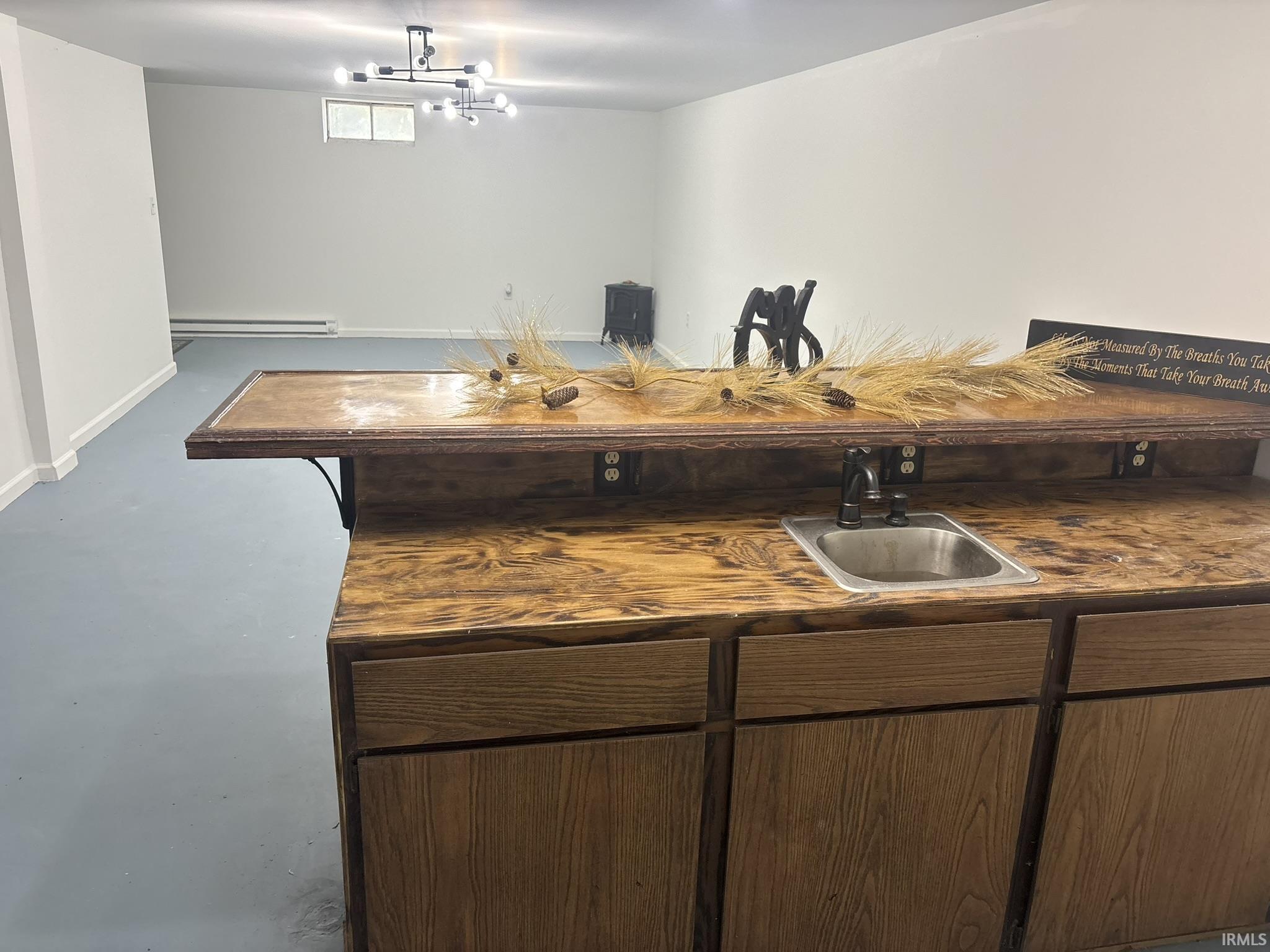 Spacious open room featuring a built-in wet bar with a stainless steel sink, wood-finish cabinetry, and an overhead shelf