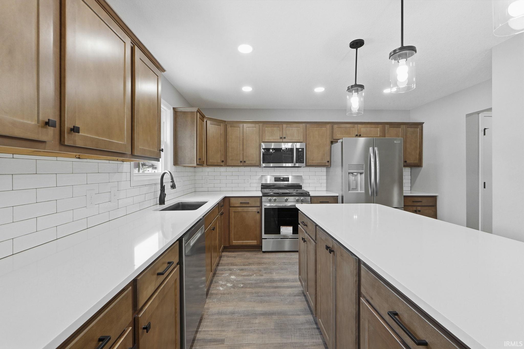 Kitchen featuring wood finish cabinets, stainless steel appliances, pendant lighting, dark wood-style floors, and tasteful backsplash