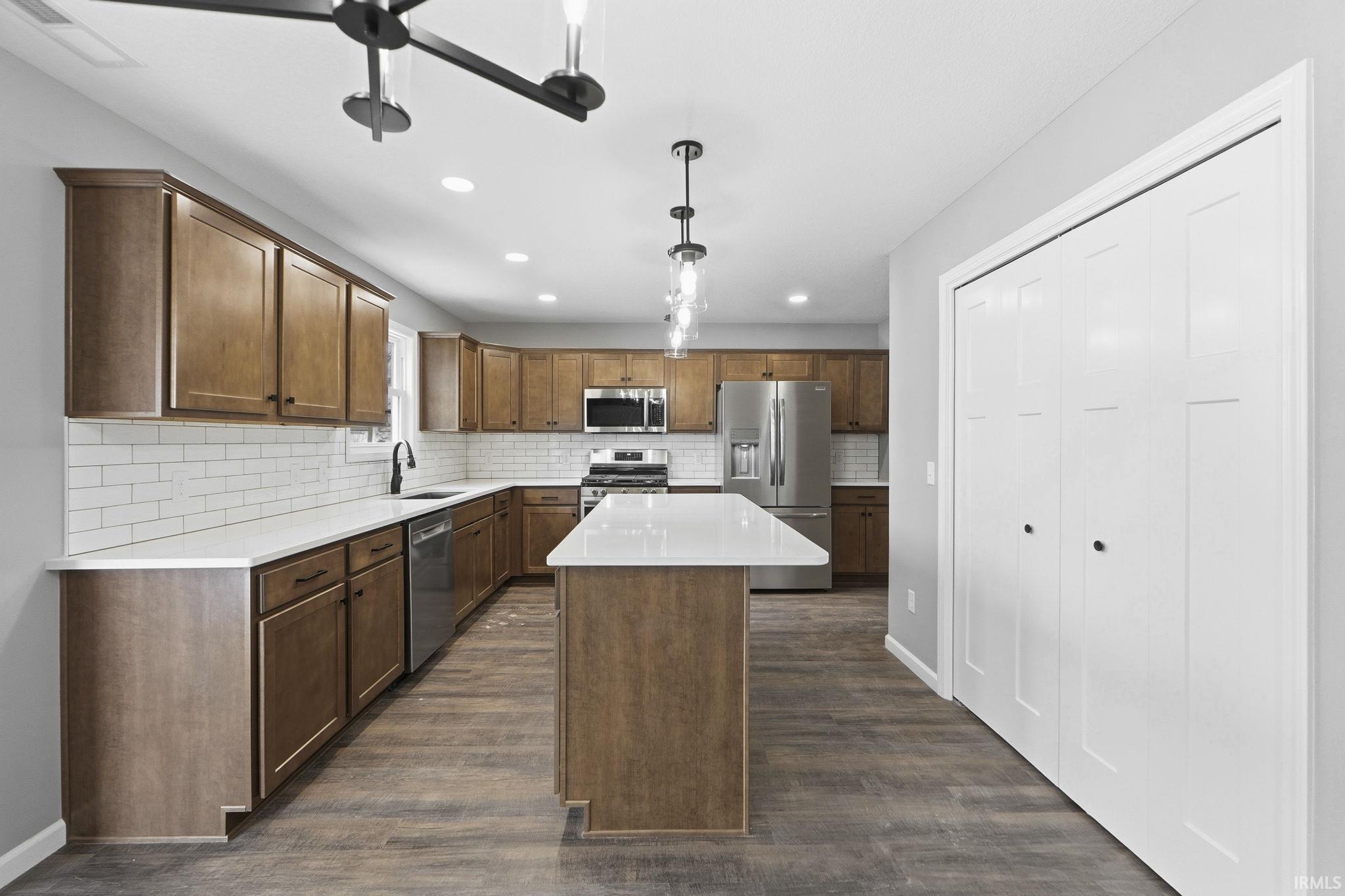 Kitchen with a center island, stainless steel appliances, decorative backsplash, pendant lighting, and dark wood-type flooring