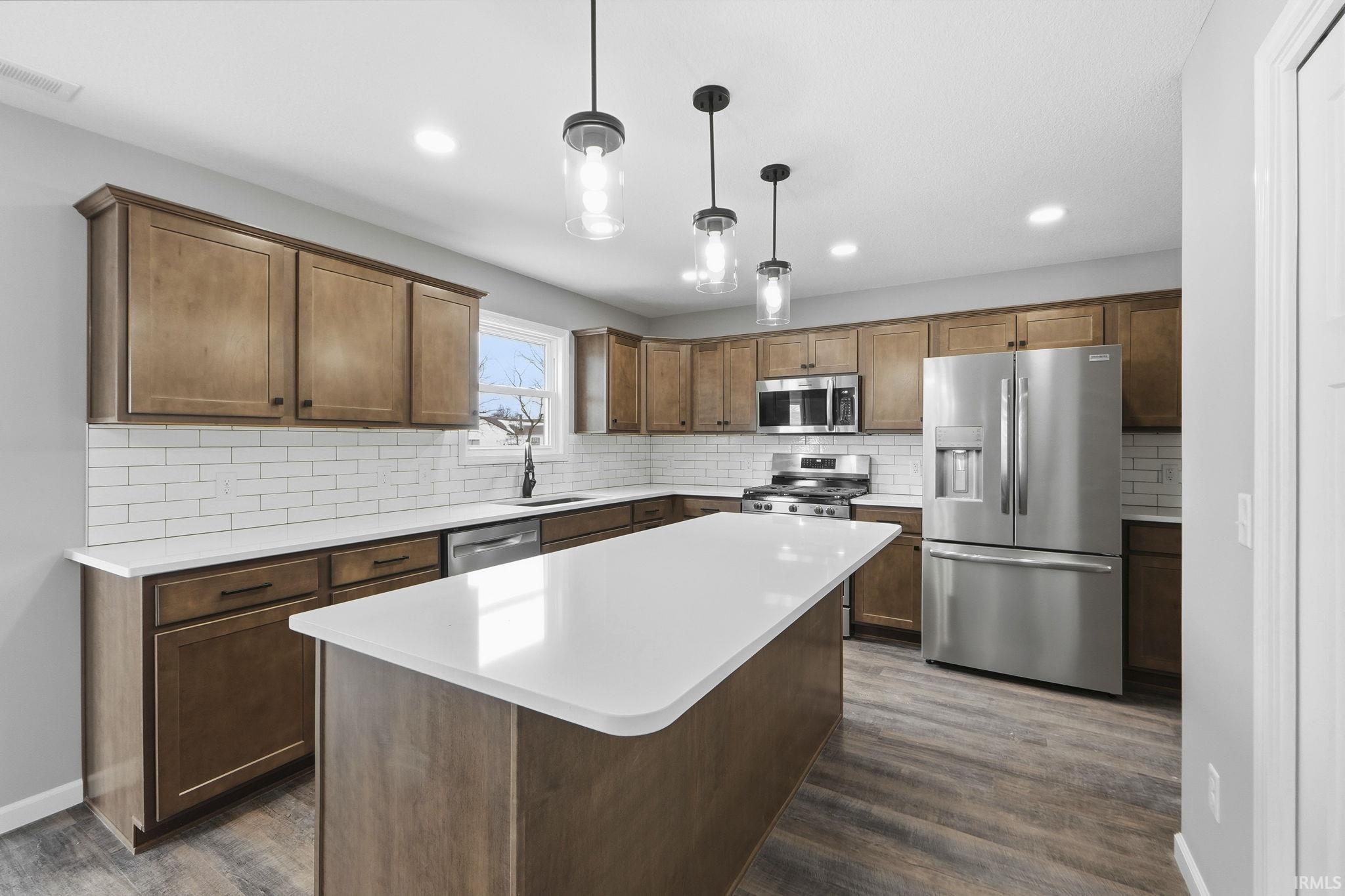 Kitchen featuring stainless steel appliances, pendant lighting, a kitchen island, and dark wood-type flooring