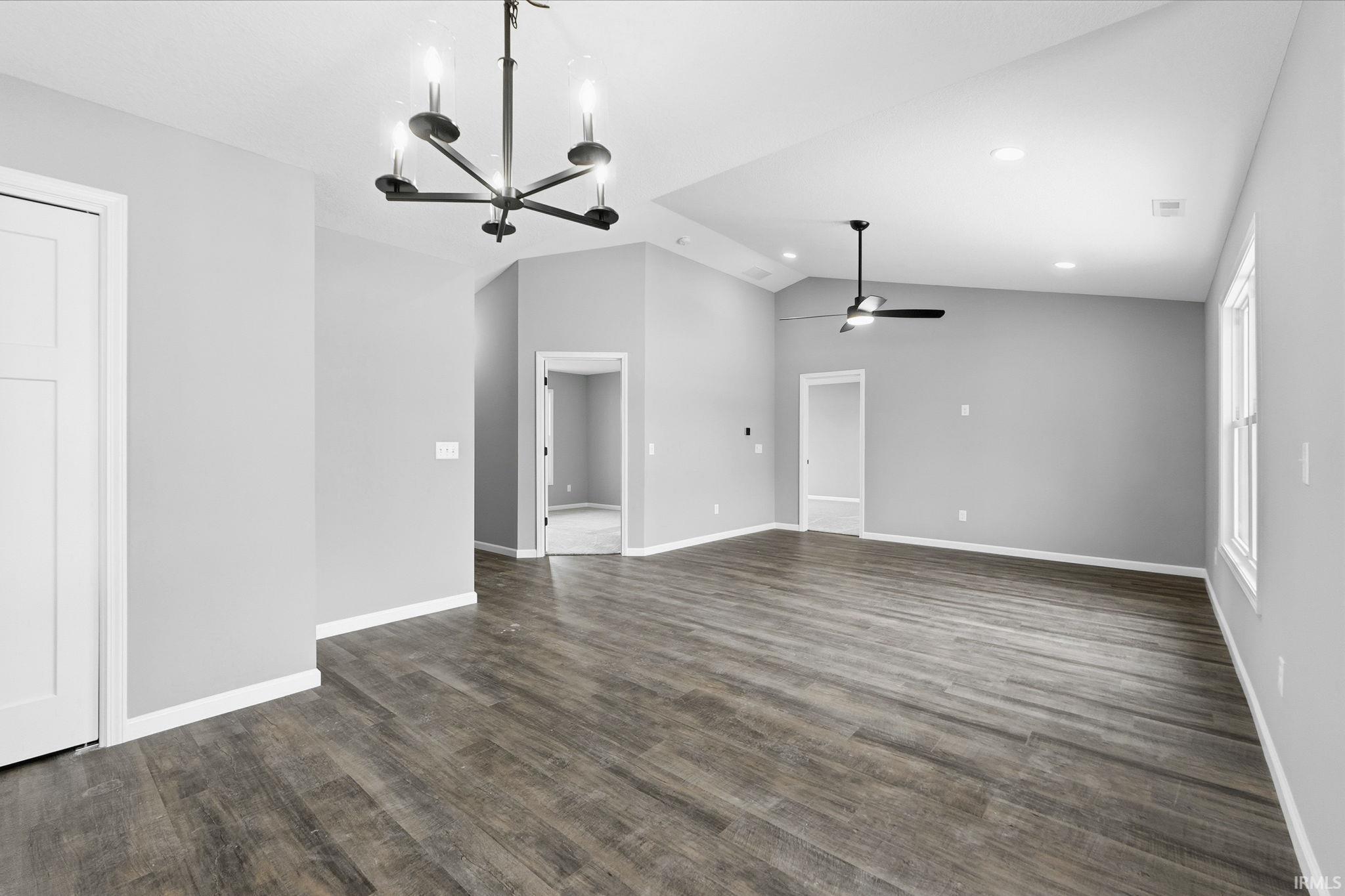 Unfurnished living room featuring lofted ceiling, a chandelier, dark wood-style floors, and a ceiling fan