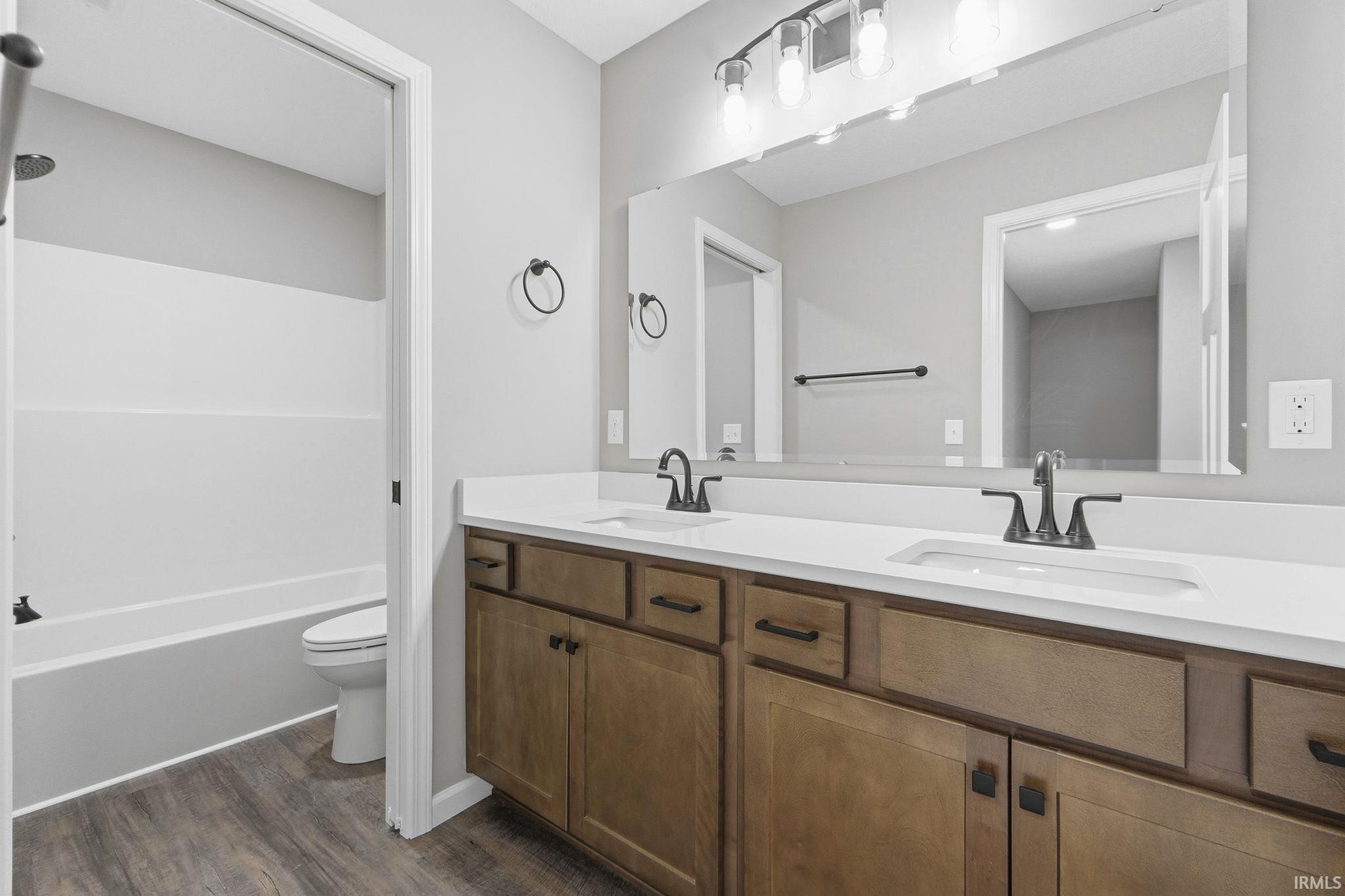 Full bathroom with double vanity, bathing tub / shower combination, and dark wood-style flooring
