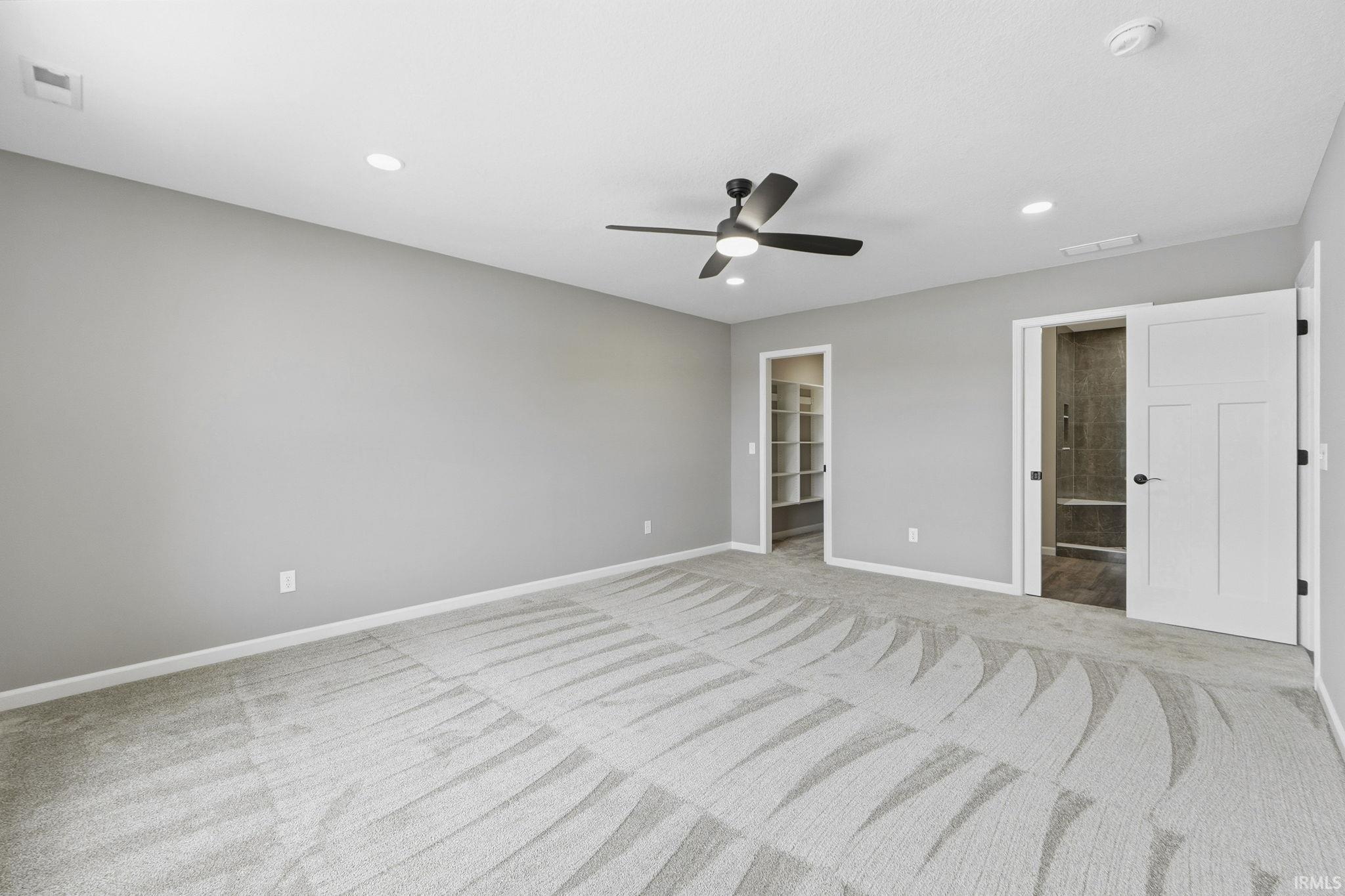 Unfurnished bedroom featuring a spacious closet, light colored carpet, recessed lighting, a ceiling fan, and ensuite bath