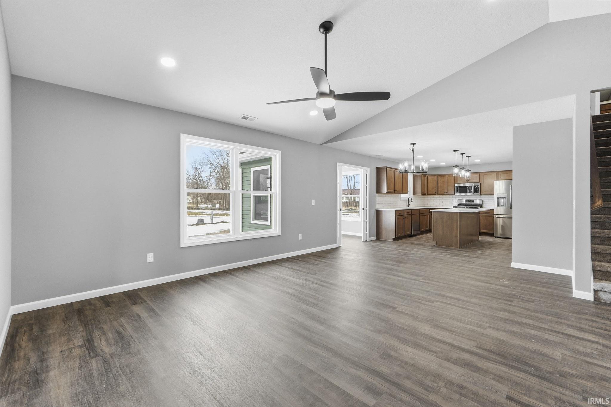 Unfurnished living room featuring hanging lights, ceiling fan, lofted ceiling, and dark wood-type flooring