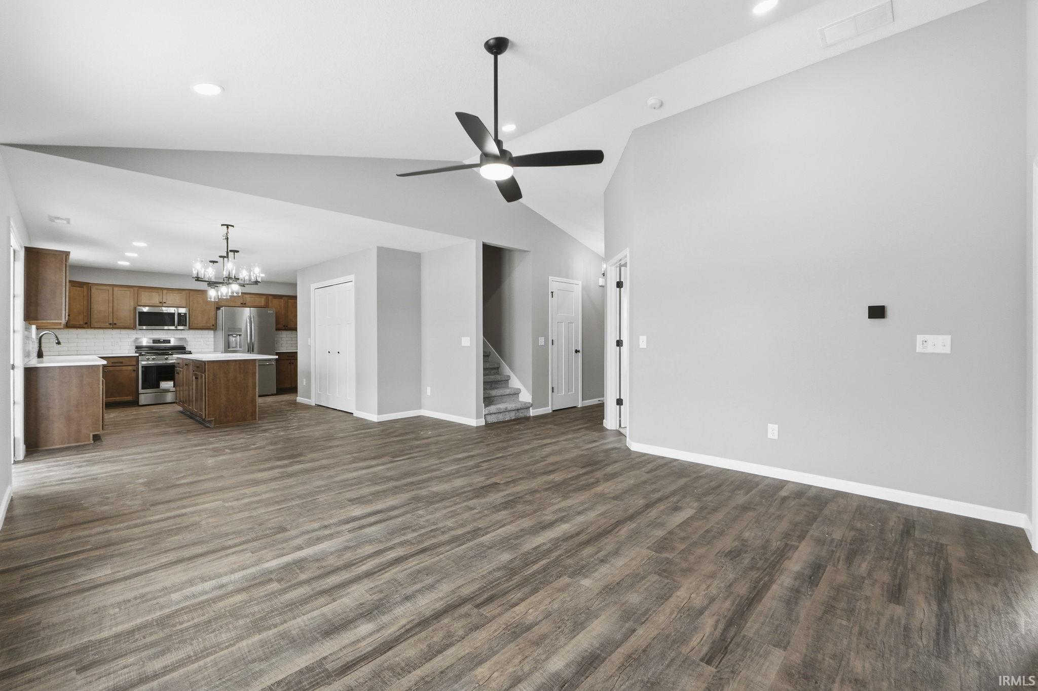 Unfurnished living room featuring hanging lights, ceiling fan, lofted ceiling, and dark wood-style floors