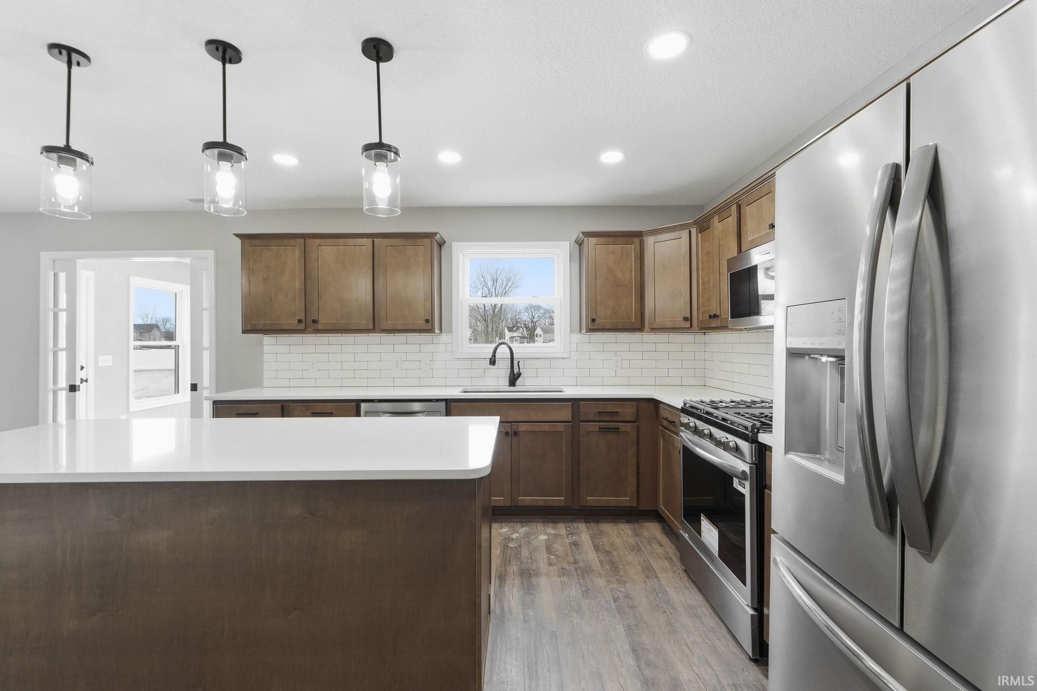 Kitchen with stainless steel appliances, decorative light fixtures, decorative backsplash, dark wood-type flooring, and a center island