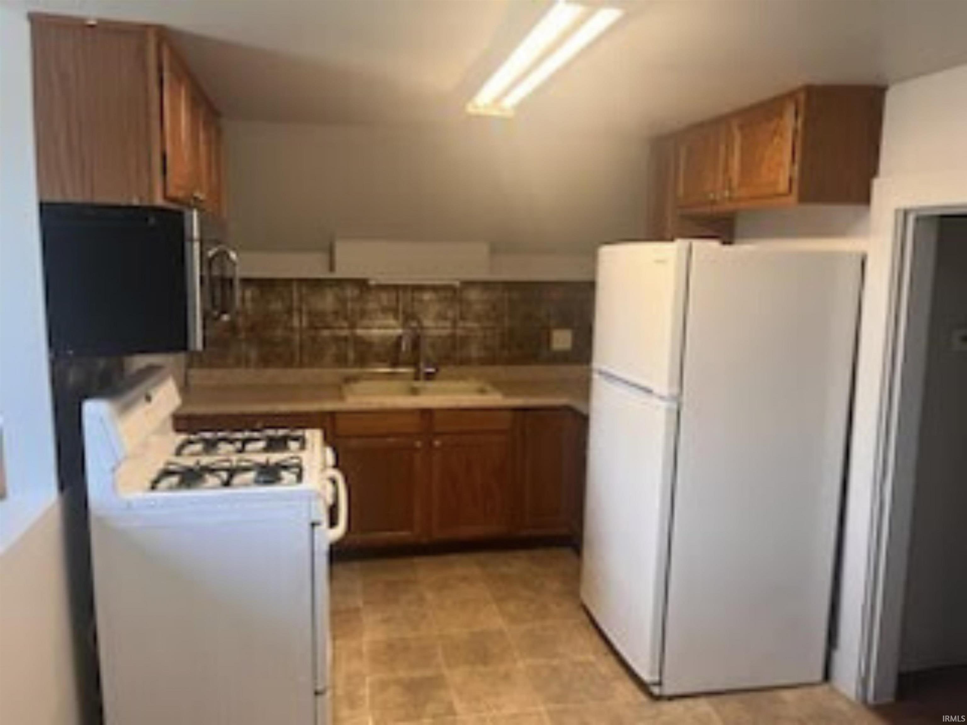 Kitchen with white appliances, wood finish cabinets, light countertops, and decorative backsplash