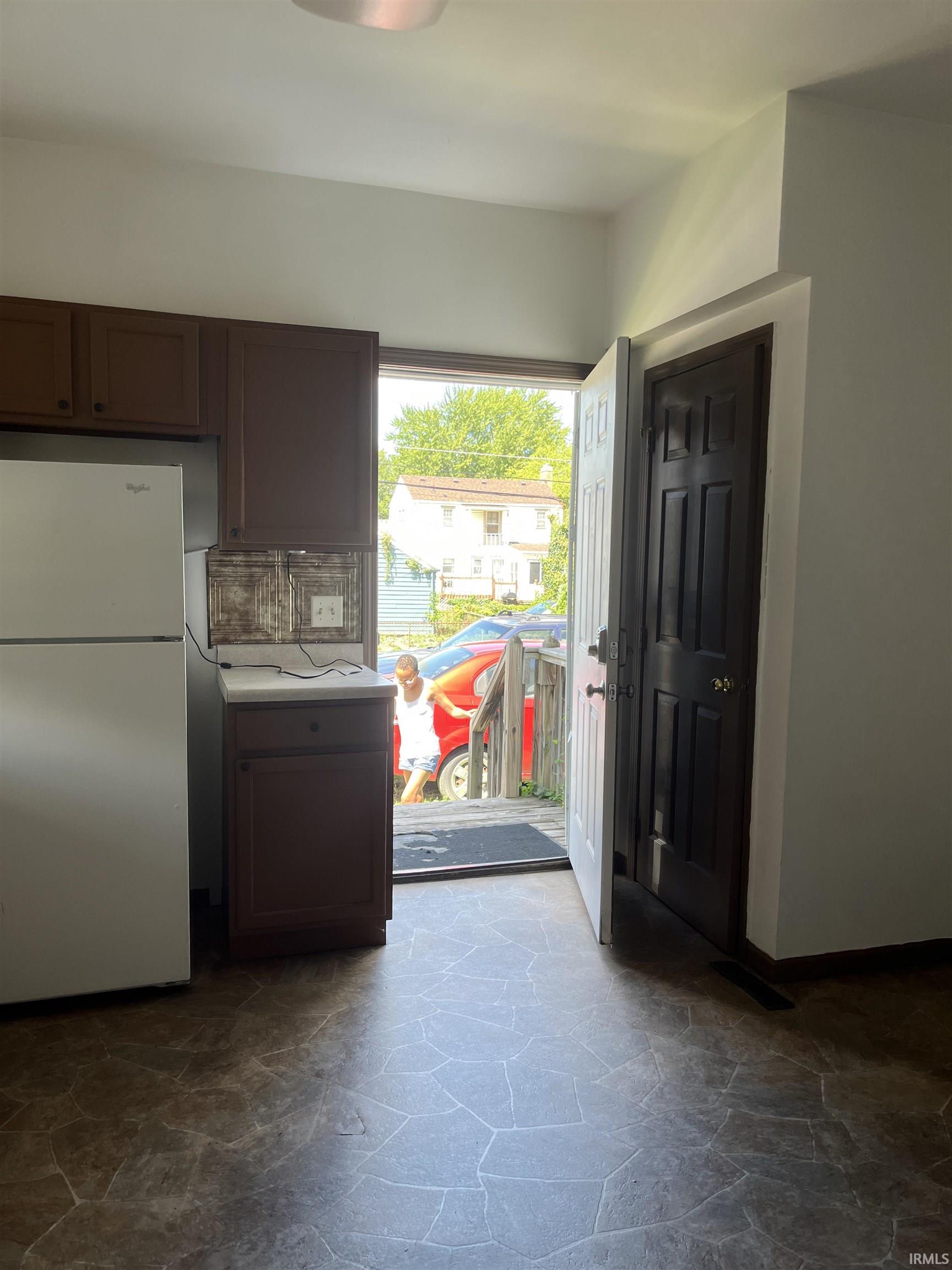 Kitchen with freestanding refrigerator, stone flooring, light countertops, dark wood finish cabinetry, and tasteful backsplash