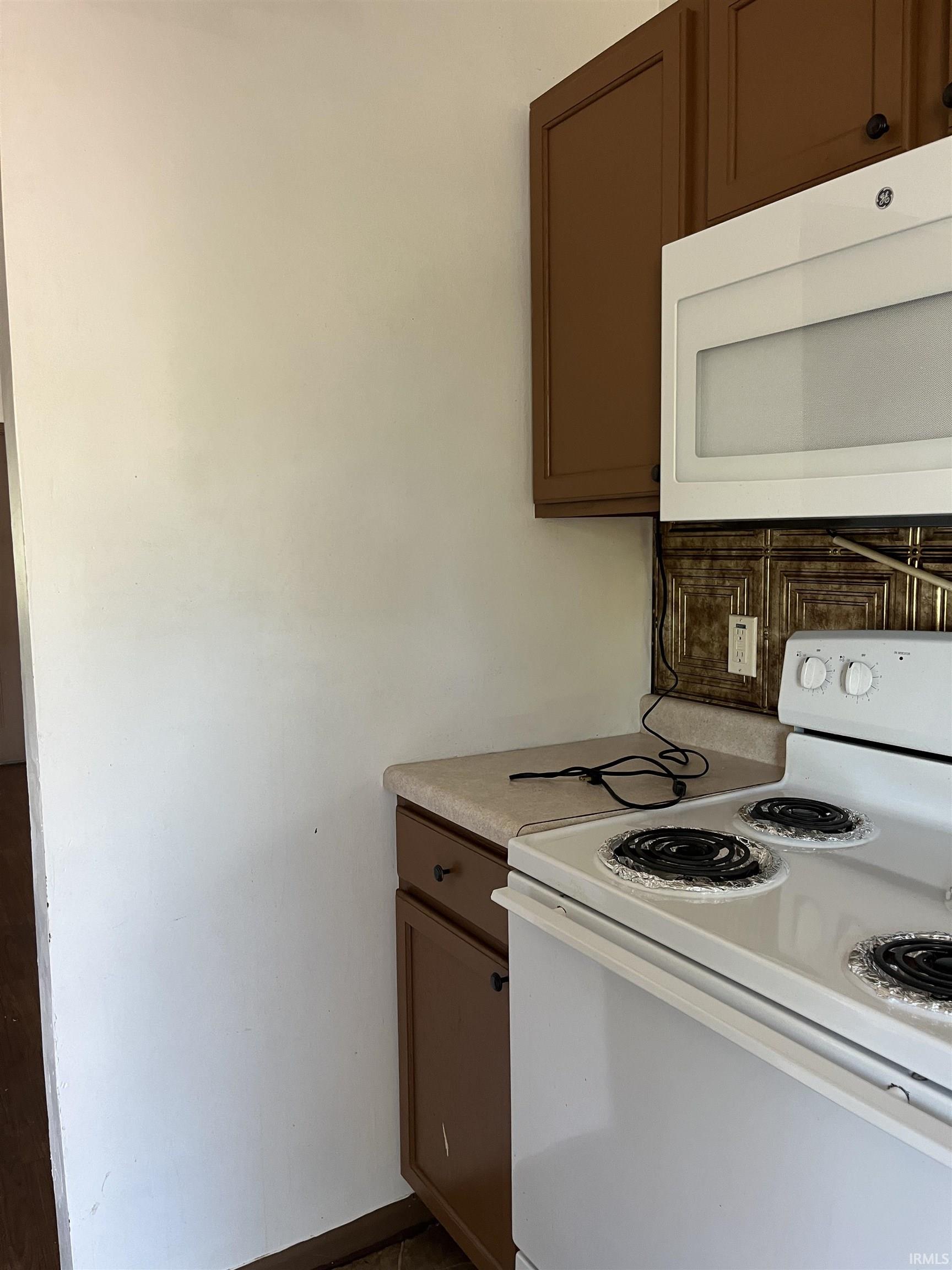 Kitchen featuring white appliances, light countertops, backsplash, and dark wood finish cabinetry