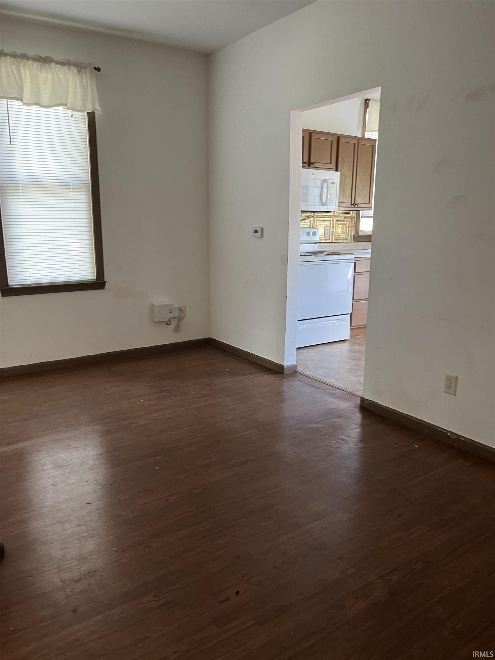 Spare room with dark wood-type flooring and baseboards