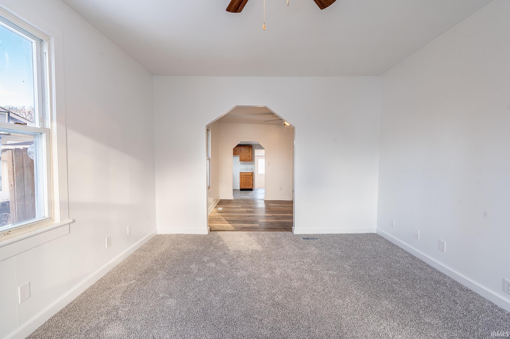 Carpeted spare room featuring a ceiling fan and arched walkways
