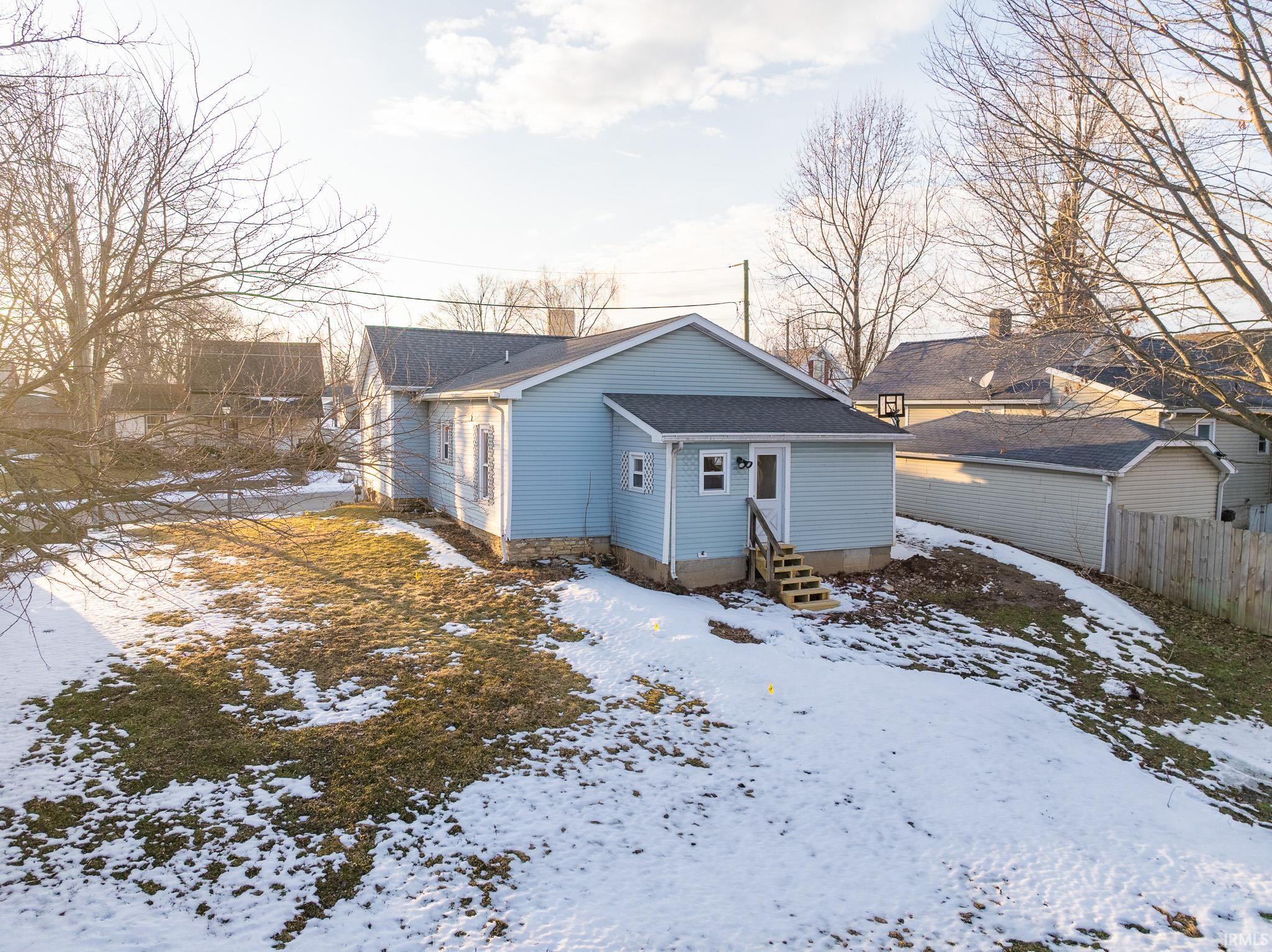 Snow covered back of property featuring entry steps and a shingled roof