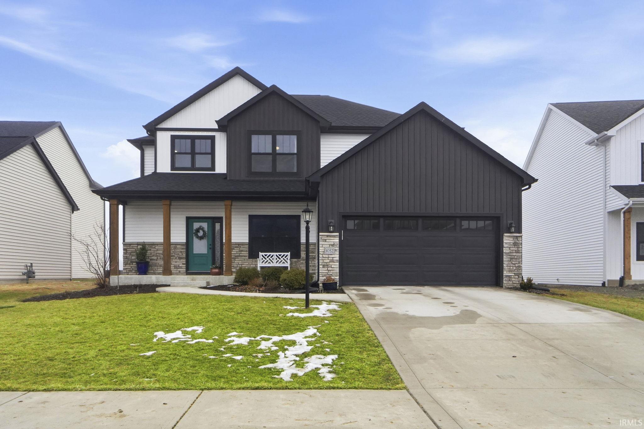 Modern inspired farmhouse featuring a porch, concrete driveway, stone siding, and a front lawn